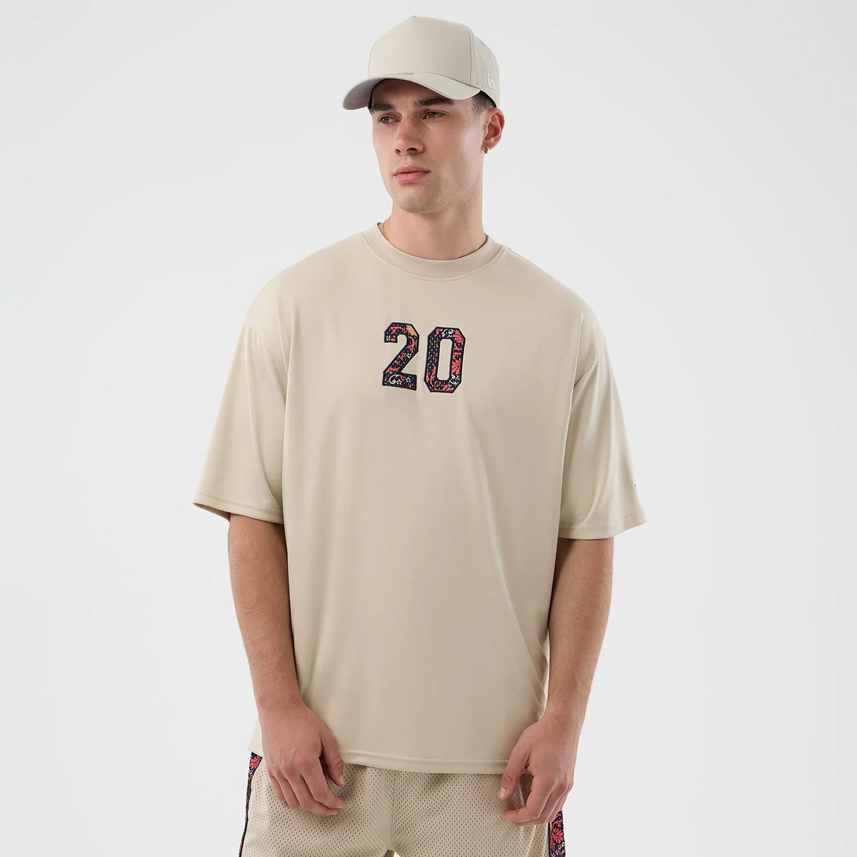 New Era Mesh Infill Light Beige Oversized T-Shirt, front view on-model showing the oversized fit and the number 20 with a coloured mesh infill design prominently embroidered on the chest.