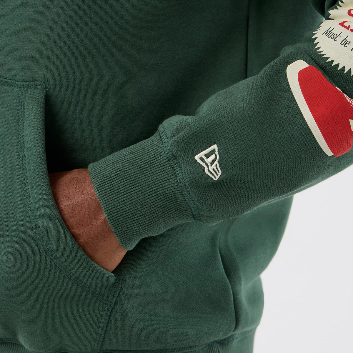 New Era A Christmas Story Major Award Dark Green Pullover Hoodie, on-model view showing the dark green sleeve with a printed red and cream graphic, an embroidered New Era logo near the cuff, and a glimpse of the front pocket.