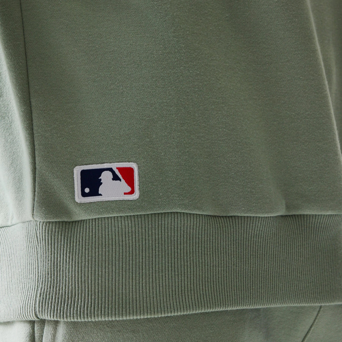 New Era LA Dodgers MLB Midi Pastel Green Oversized Crew Neck Sweater, close-up showing the embroidered MLB logo on the ribbed hem, highlighting the soft pastel green fabric and the sweater's relaxed fit style.