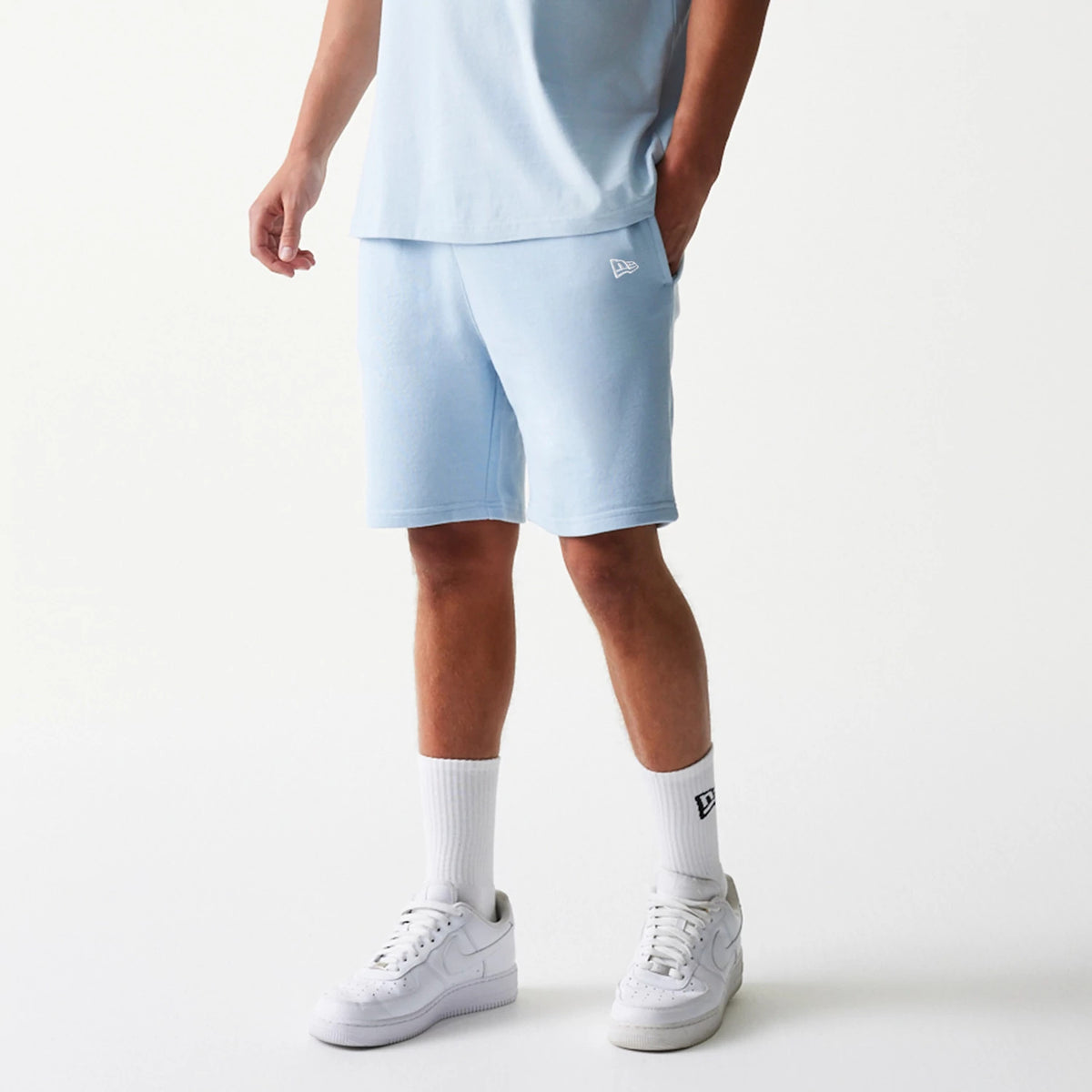 New Era New York Yankees MLB League Essential Midi Pastel Blue Shorts, front view on a model paired with a matching pastel blue top, featuring an embroidered New Era logo on the left leg above the hem.