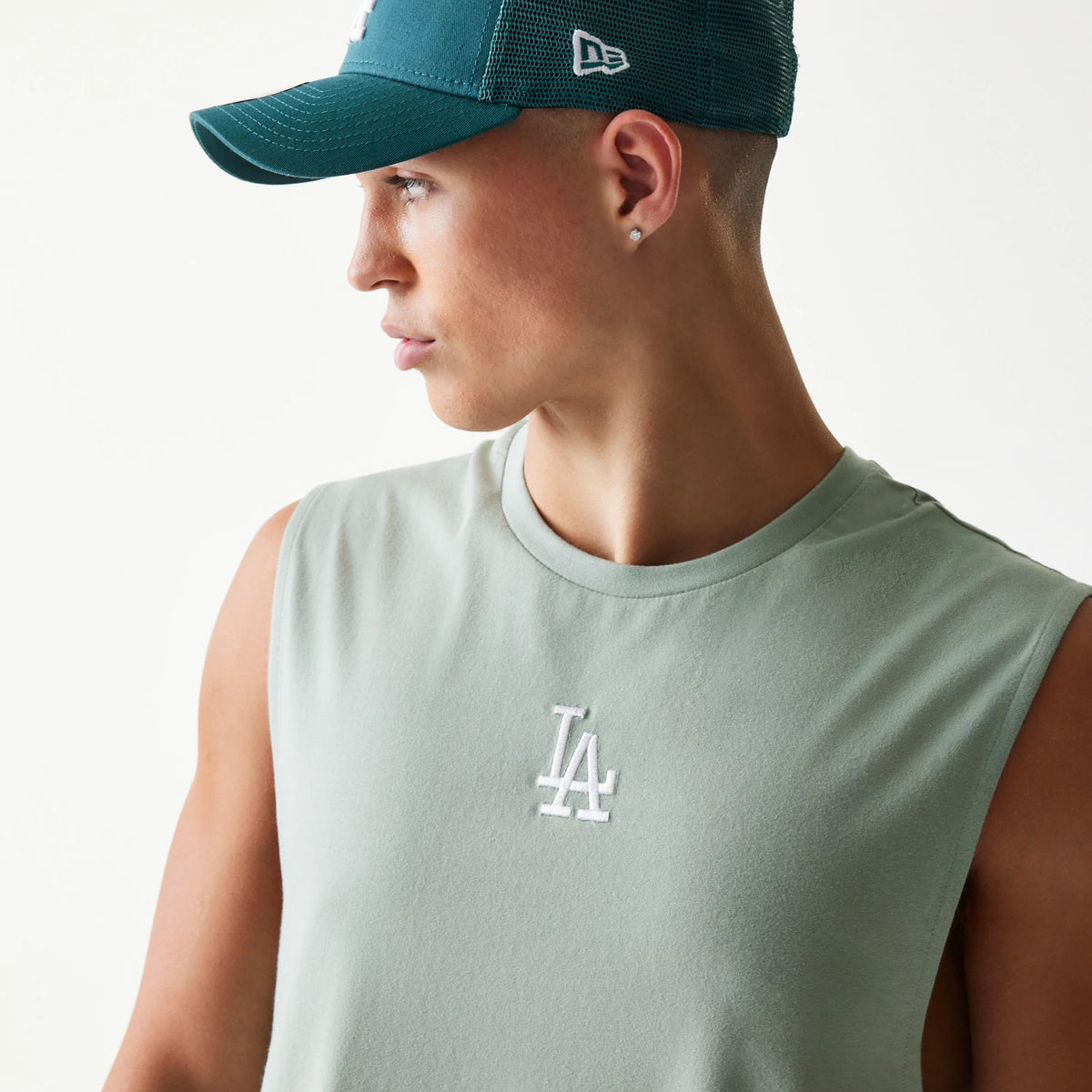 New Era LA Dodgers MLB Pastel Green Sleeveless T-Shirt, front three-quarter view showing the pastel green sleeveless design with a white embroidered LA logo on the chest, styled on a model wearing a dark teal New Era cap.