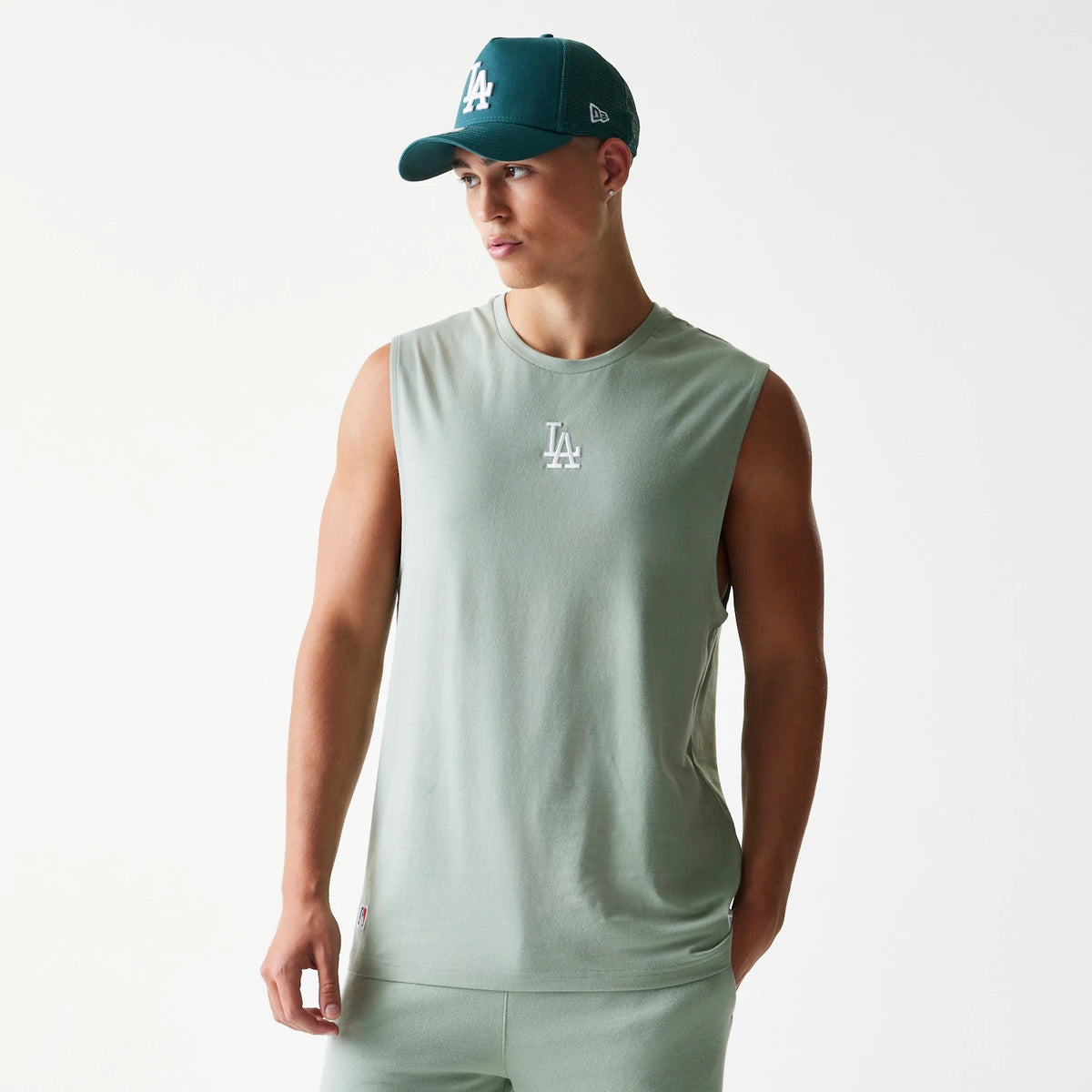 New Era LA Dodgers MLB Pastel Green Sleeveless T-Shirt, front view on a model with a matching cap, featuring an embroidered white LA logo centred on the chest, highlighting the relaxed sleeveless fit in a soft pastel green shade.