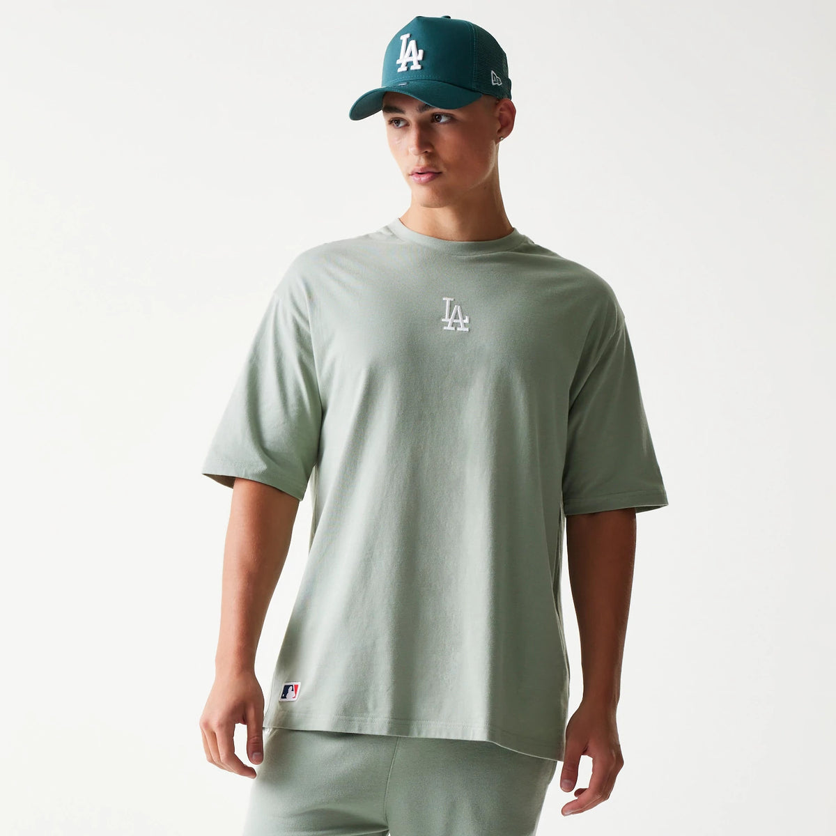 New Era LA Dodgers MLB Midi Pastel Green Oversized T-Shirt, front view on-model showing a white printed LA logo centred on the chest and a small MLB logo near the bottom hem, paired with a matching cap.