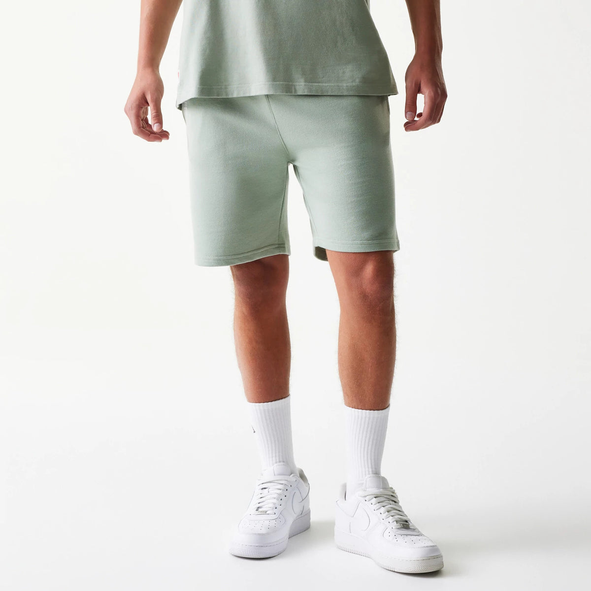 New Era LA Dodgers MLB League Essential Midi Pastel Green Shorts, front view on a model styled with white trainers and socks, showing the knee-length pastel green shorts with a clean finish and no logo details.
