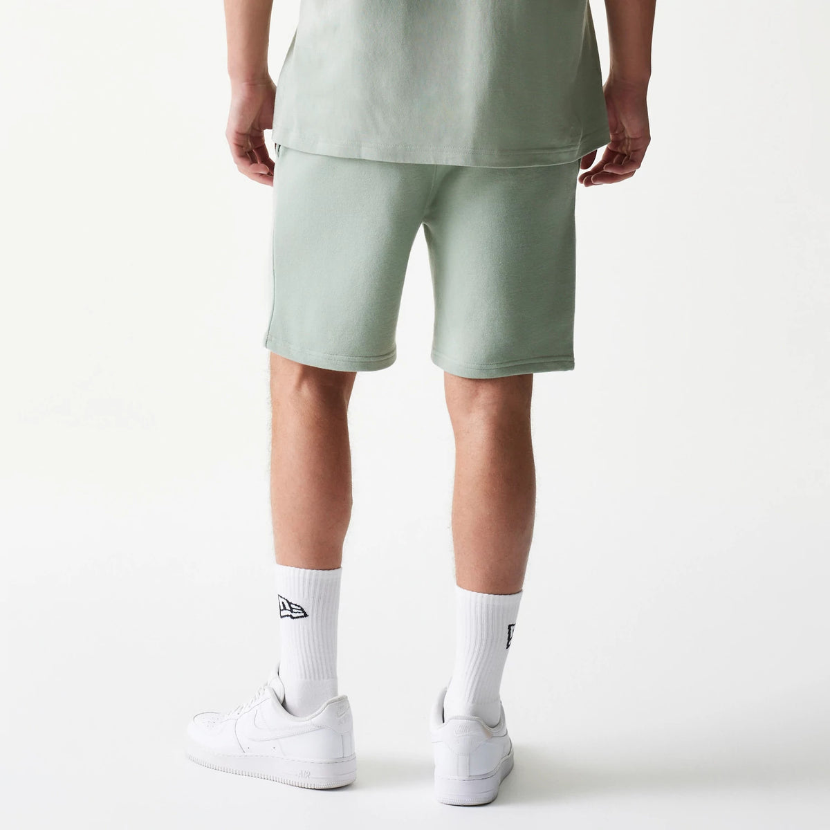 New Era LA Dodgers MLB League Essential Midi Pastel Green Shorts, back view on a model styled with a pastel green top and white trainers showing the simple design of the pastel green shorts extending just above the knee.