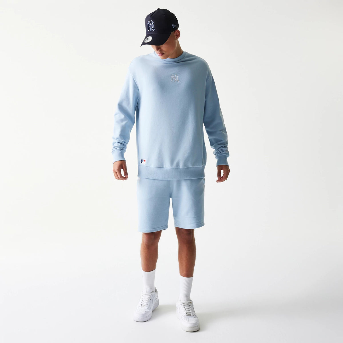 New Era New York Yankees MLB Midi Blue Oversized Crew Neck Sweater, on-model front view showing the white NY logo embroidered on the chest, teamed with matching blue shorts, white socks, and trainers.