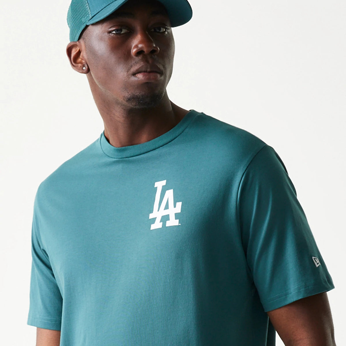 New Era LA Dodgers MLB Food Graphic Dark Green T-Shirt, front view on a model showcasing a white printed LA logo on the left chest, with the New Era logo embroidered on the left sleeve, styled with a matching cap.