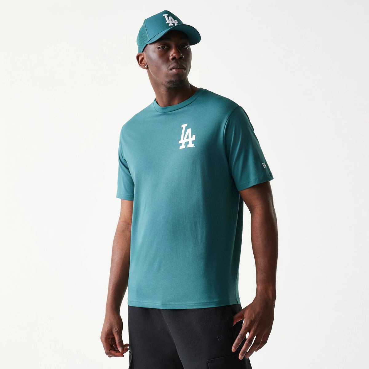 New Era LA Dodgers MLB Food Graphic Dark Green T-Shirt, front view on-model showing a white embroidered LA logo on the left chest, styled with a matching cap and black trousers, capturing a casual look.