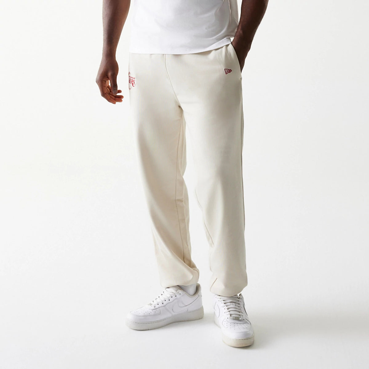 New Era LA Lakers NBA League Essential Cream Joggers, front view on a model showing LA Lakers logo embroidered in red on the right thigh, with pockets and a relaxed fit, paired with white trainers and a plain white T-shirt.