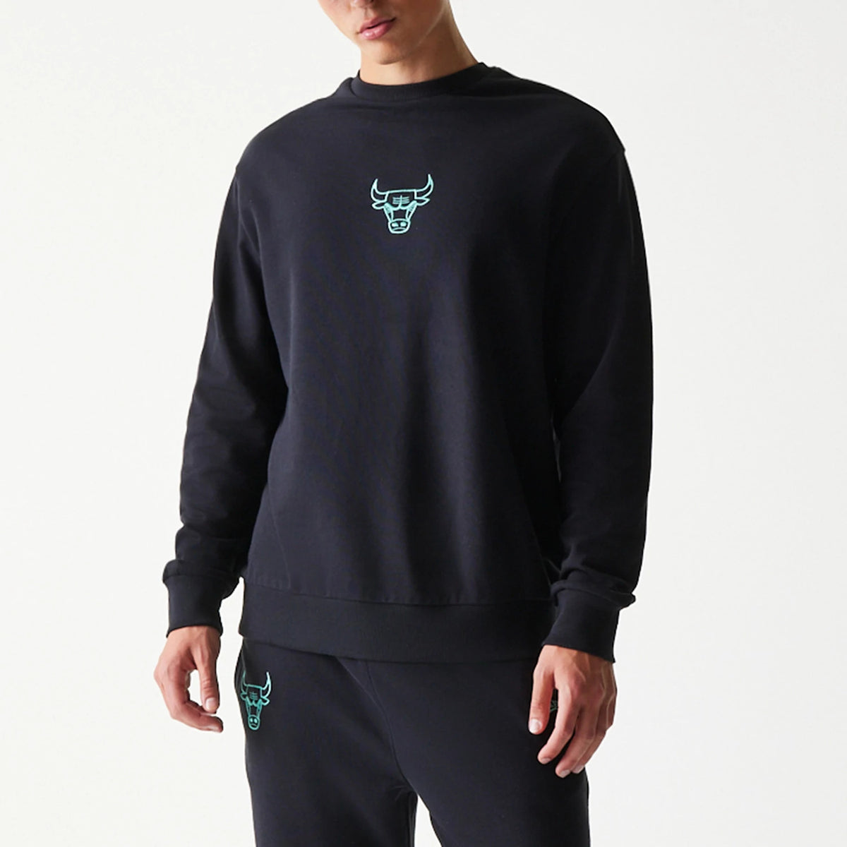 New Era Chicago Bulls NBA Black Oversized Crew Neck Sweater, front view on a model with a teal Chicago Bulls logo embroidered on the upper chest, showcasing the relaxed fit and ribbed cuffs of the black sweater.