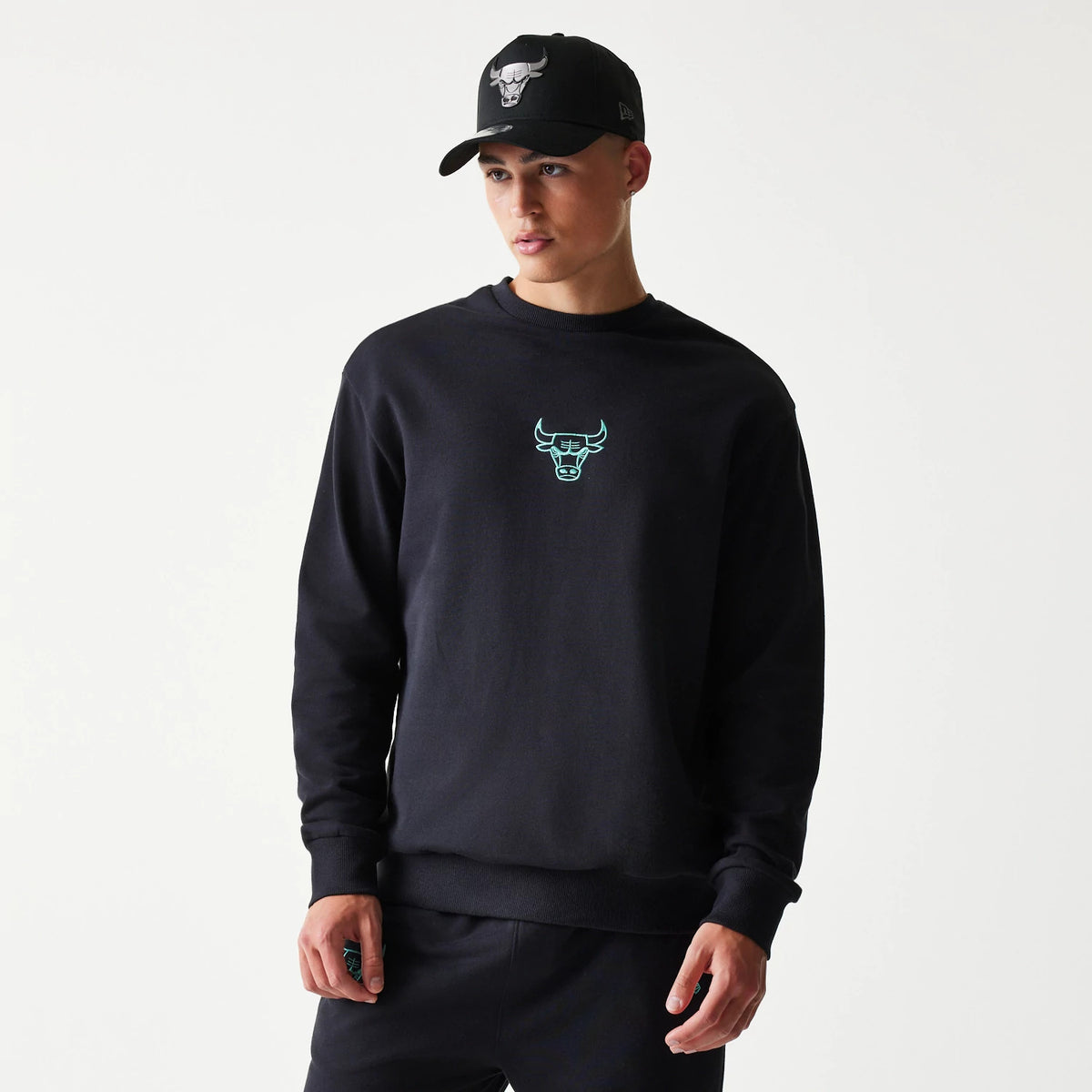 New Era Chicago Bulls NBA Black Oversized Crew Neck Sweater, front view on a model with a matching cap, featuring a light blue embroidered Bulls logo centred on the chest of the black long-sleeve sweater.