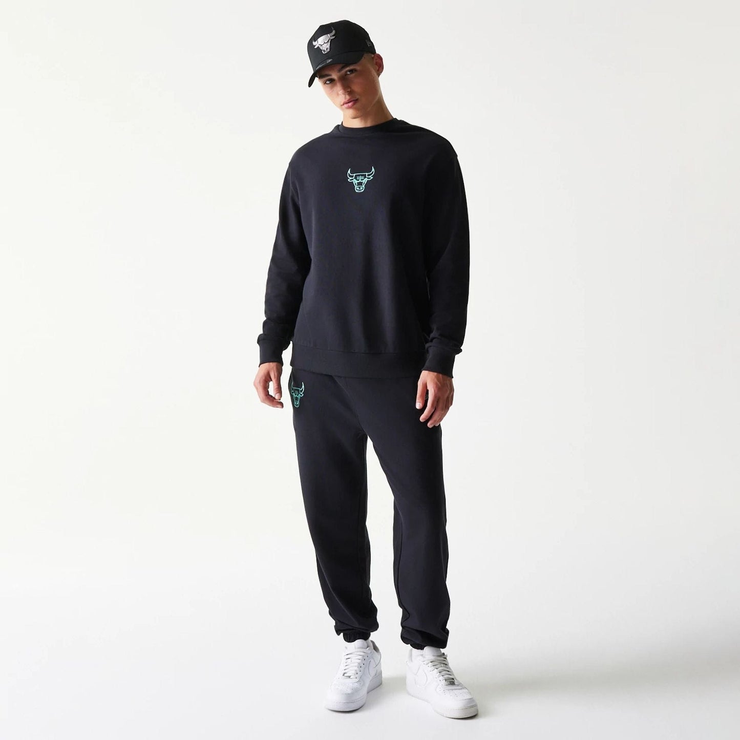 New Era Chicago Bulls NBA Black Oversized Crew Neck Sweater, front view on a model with a matching cap, featuring a teal embroidered Bulls logo on the chest, long sleeves and a relaxed fit for casual sportswear styling.