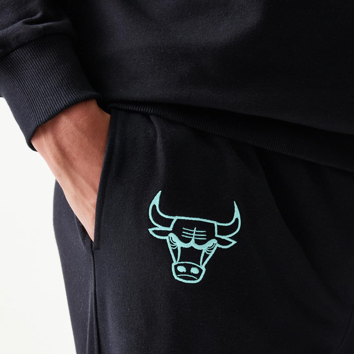 New Era Chicago Bulls NBA League Essential Black Joggers, close-up showing the light blue embroidered team logo on the left thigh above the pocket, with a ribbed cuff and a relaxed fit.