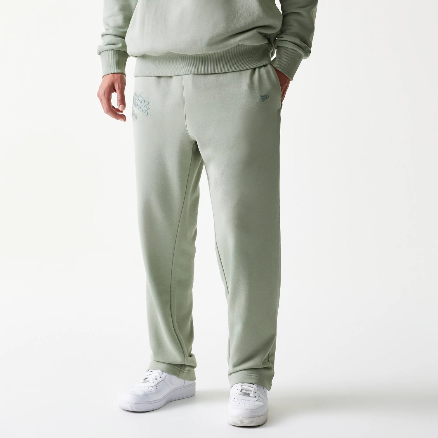 New Era LA Lakers NBA Pastel Green Straight Leg Joggers, front view on a model with hands in pockets, showing the embroidered Lakers logo on the upper left leg and a tidy finish around the ankles, paired with white trainers.