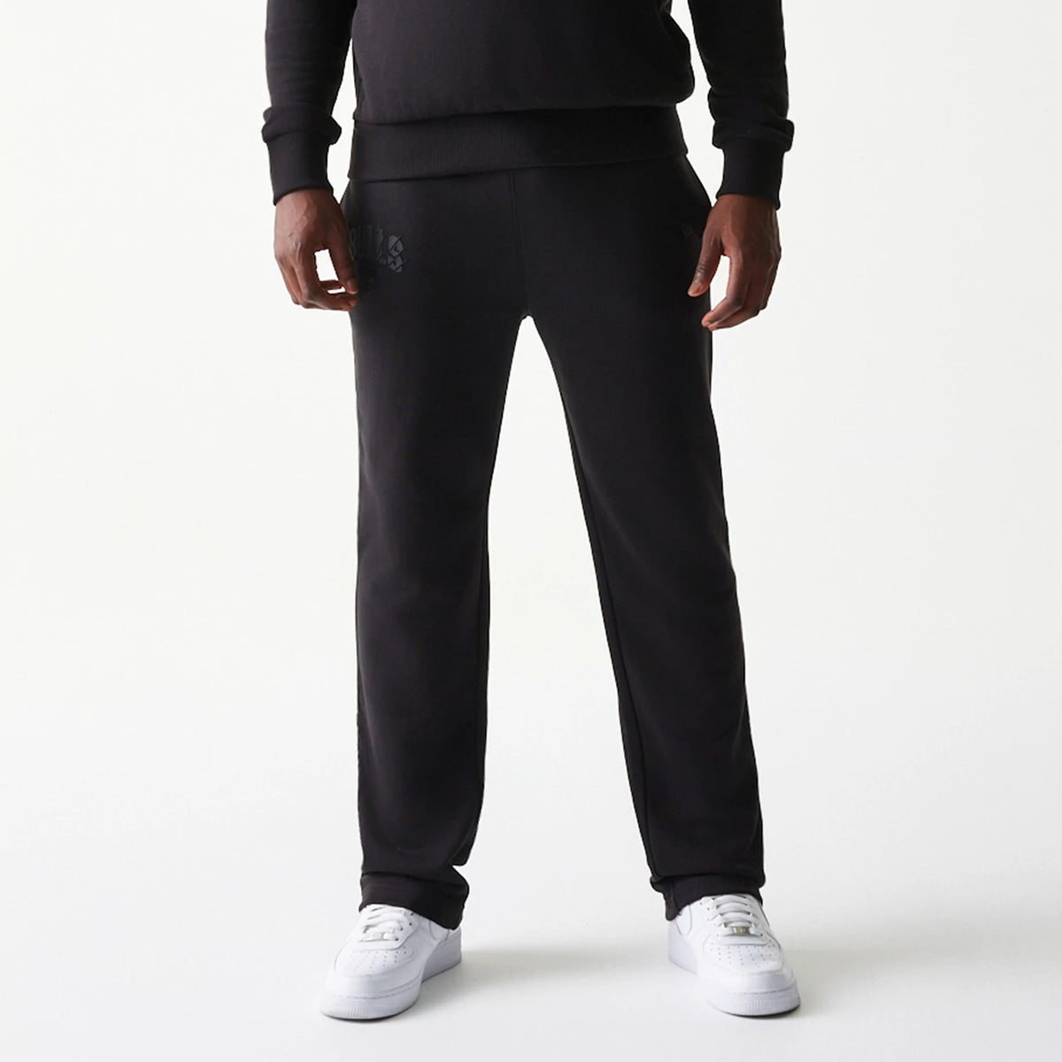 New Era Chicago Bulls NBA Black Straight Leg Joggers, front view on a model wearing white trainers, featuring the Chicago Bulls logo printed on the upper left leg, and a relaxed fit design with ribbed ankle cuffs.
