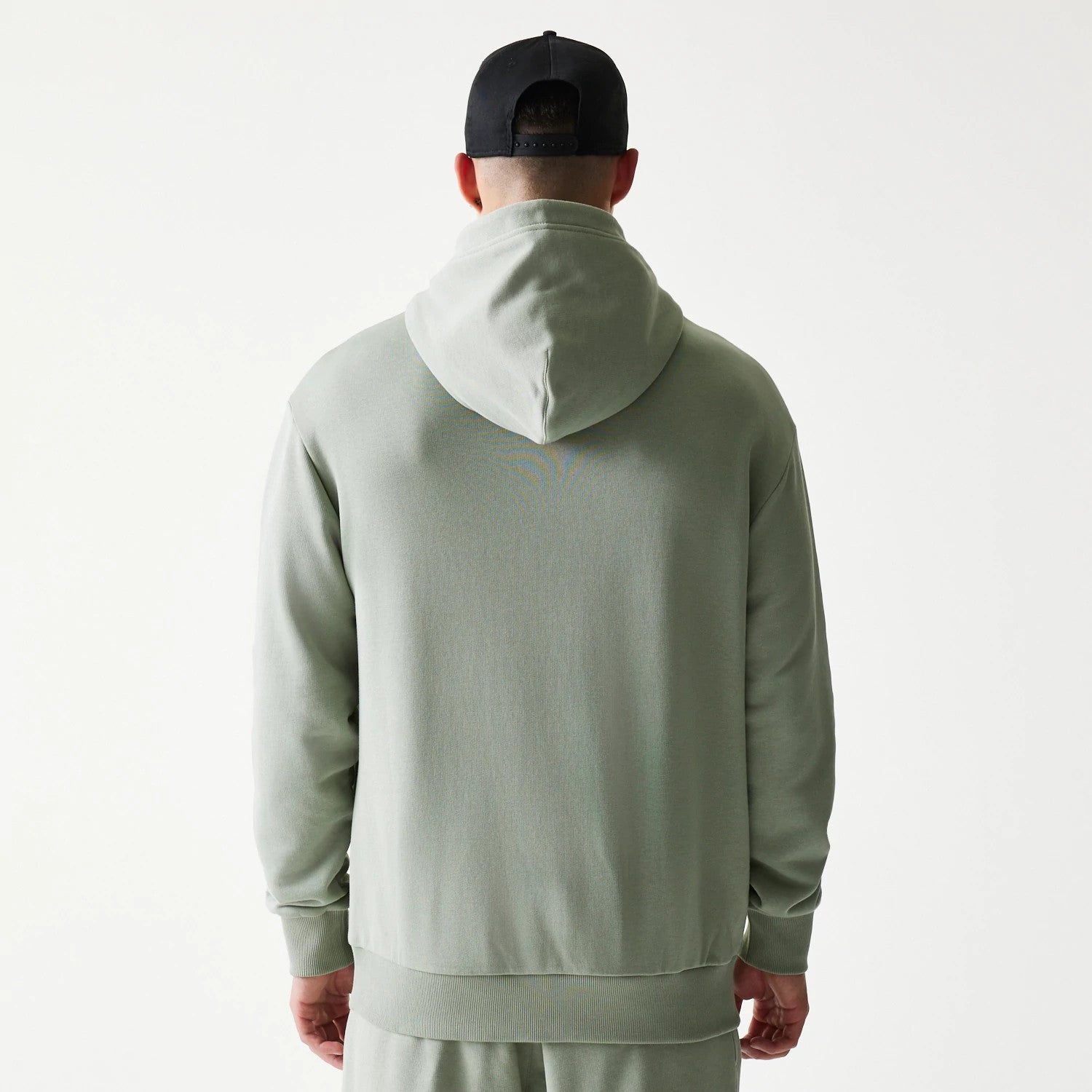 New Era LA Lakers NBA Pastel Green Oversized Pullover Hoodie, back view on a model showing the plain pastel green back with an attached hood, ribbed cuffs and hem, paired with matching trousers and a black cap.