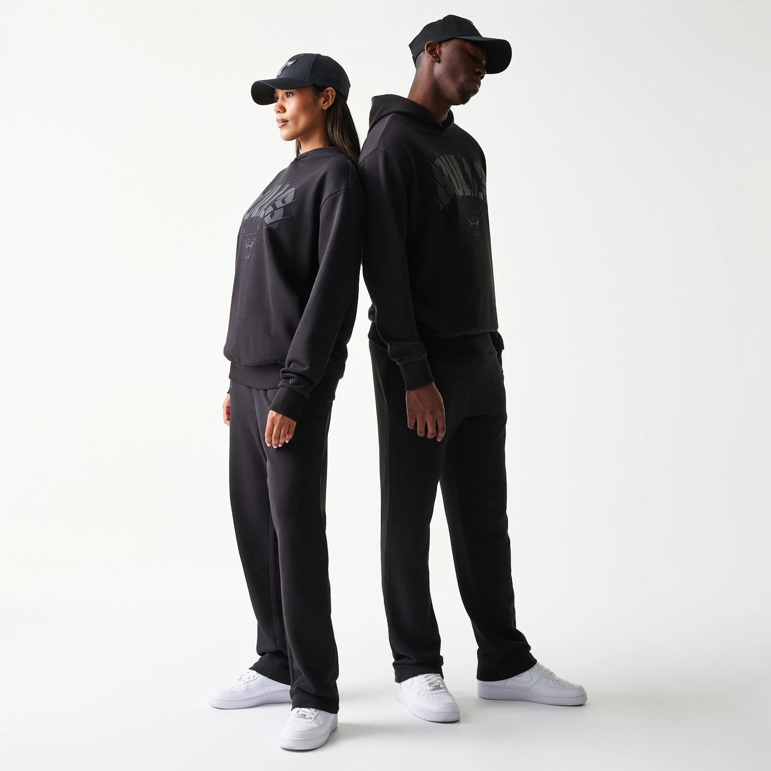 New Era Chicago Bulls NBA Black Oversized Pullover Hoodie, three-quarter view on-model showing the black hoodie with an embroidered Bulls logo on the chest, styled with matching black trousers and white trainers.