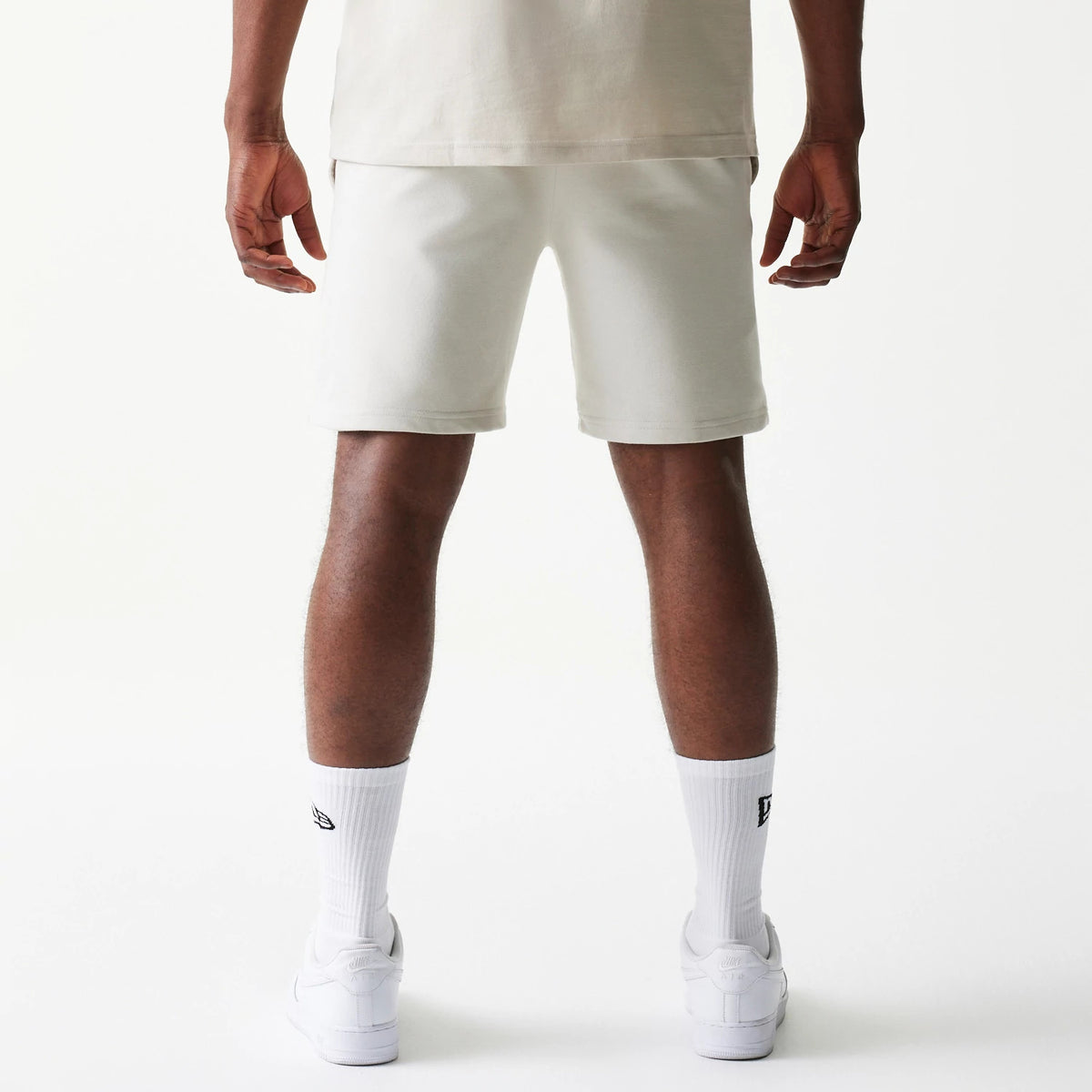 New Era LA Lakers NBA League Essential Cream Shorts, back view on a model showing the plain cream design with an elastic waistband, styled with white socks and trainers for a casual look.