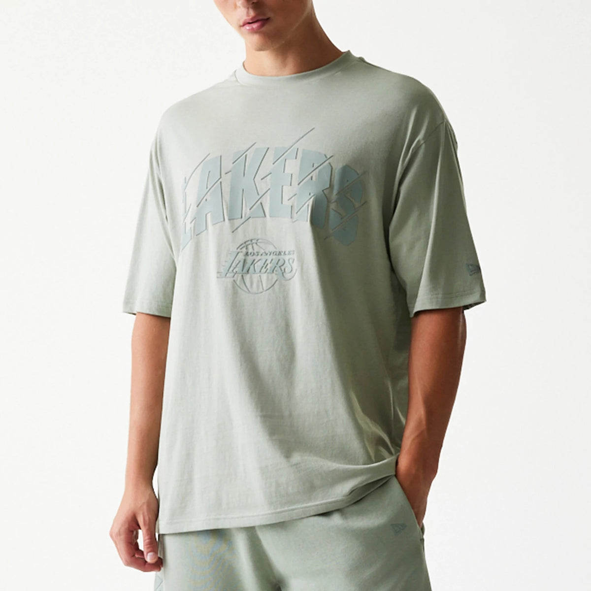 New Era LA Lakers NBA Pastel Green Oversized T-Shirt, front view on a model showing a large printed Lakers logo across the chest, small Los Angeles Lakers emblem underneath, and a New Era logo on the left sleeve.