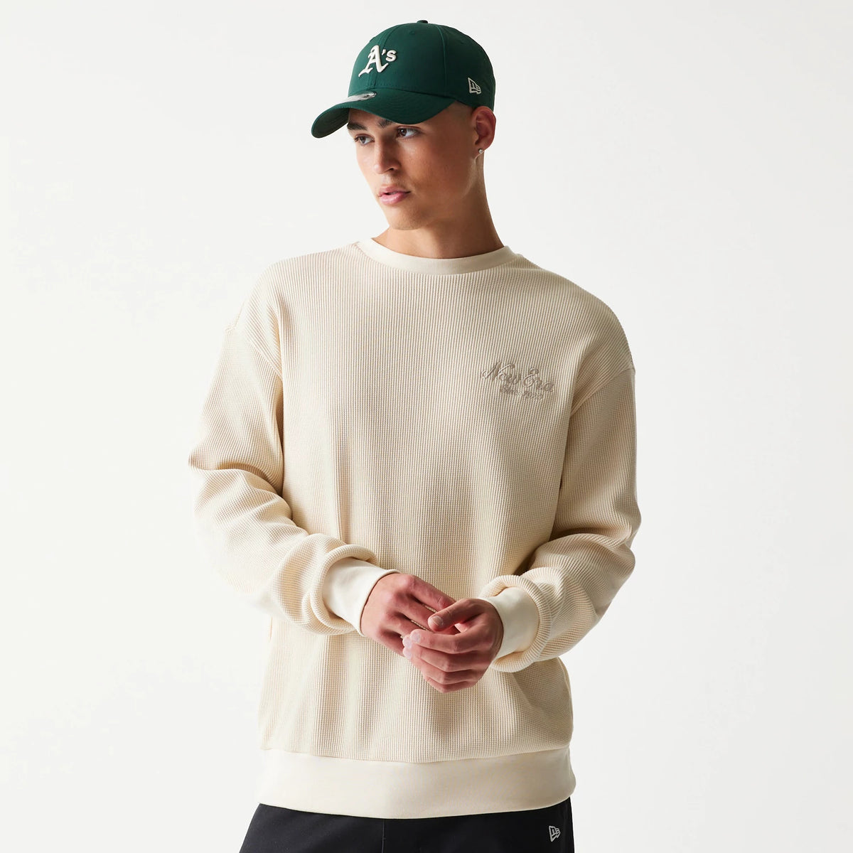 New Era Script Waffle Light Beige Crew Neck Sweater, front view on a model with an A's cap featuring ribbed cuffs and hem with embroidery on the left chest, highlighting its textured waffle fabric design.