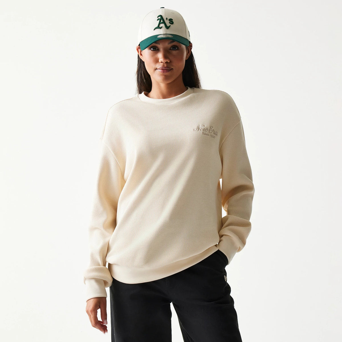 New Era Script Waffle Light Beige Crew Neck Sweater, front view on a model with a white and green cap, featuring a embroidered script logo on the chest and a textured waffle knit fabric enhancing the cosy, relaxed fit.