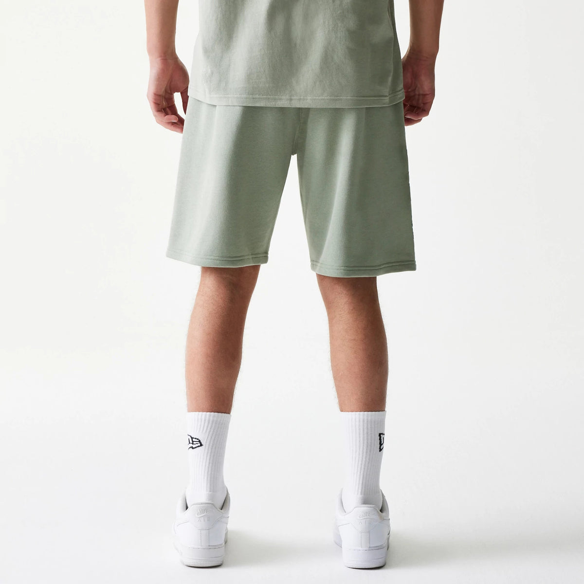 New Era LA Lakers NBA Pastel Green Shorts, back view on a model styled with a matching green top and white trainers, showing the plain design of the shorts without logos or patterns.