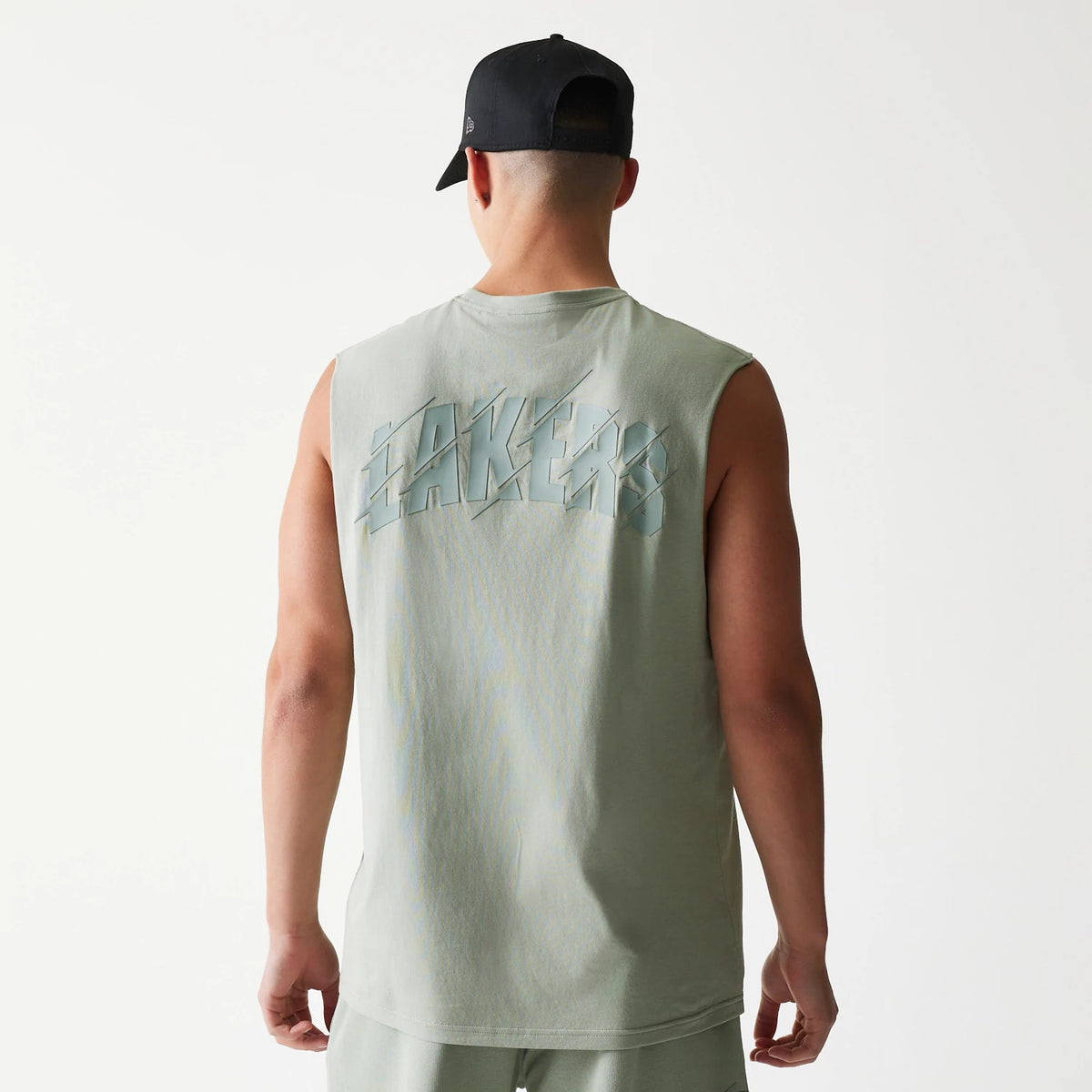 New Era LA Lakers NBA Pastel Green Sleeveless T-Shirt, back view on a model with a black cap, showcasing raised Lakers lettering across the upper back in a matching hue, and sleeveless design enhancing the relaxed fit.