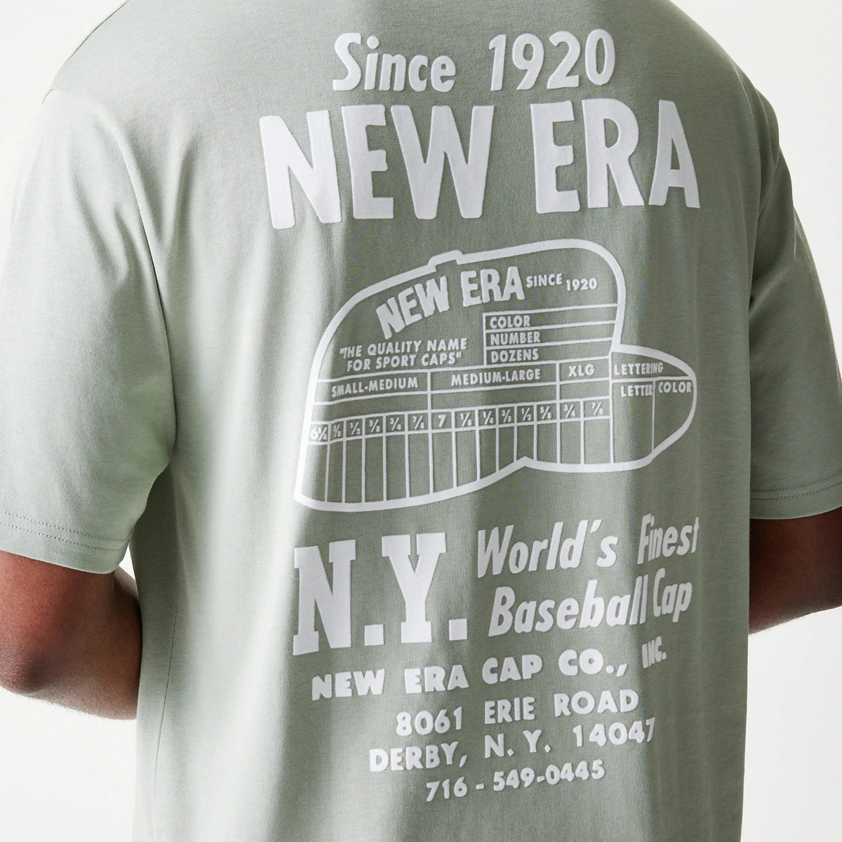 New Era Graphic Pastel Green Oversized T-Shirt, back view showing a white printed graphic with New Era branding, cap size chart illustration, and detailed address text, worn by an unseen model to highlight the design.