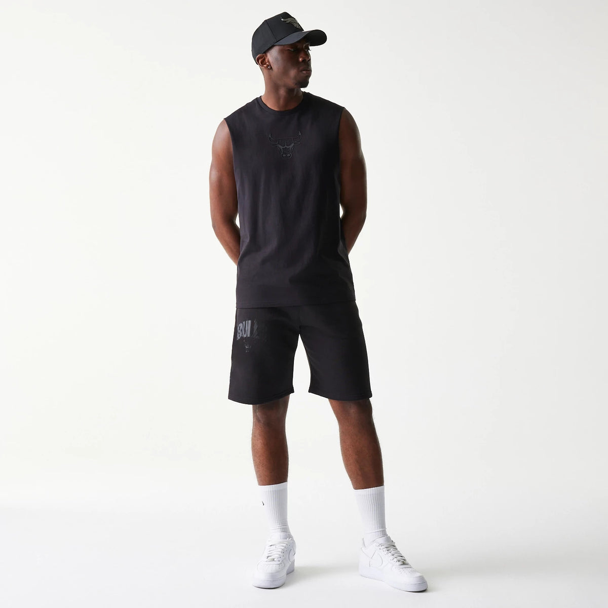 New Era Chicago Bulls NBA Black Shorts, three-quarter view on-model showing the black shorts worn with a sleeveless top and black cap, with the word Bulls printed on the left thigh and the Chicago Bulls logo embossed below.