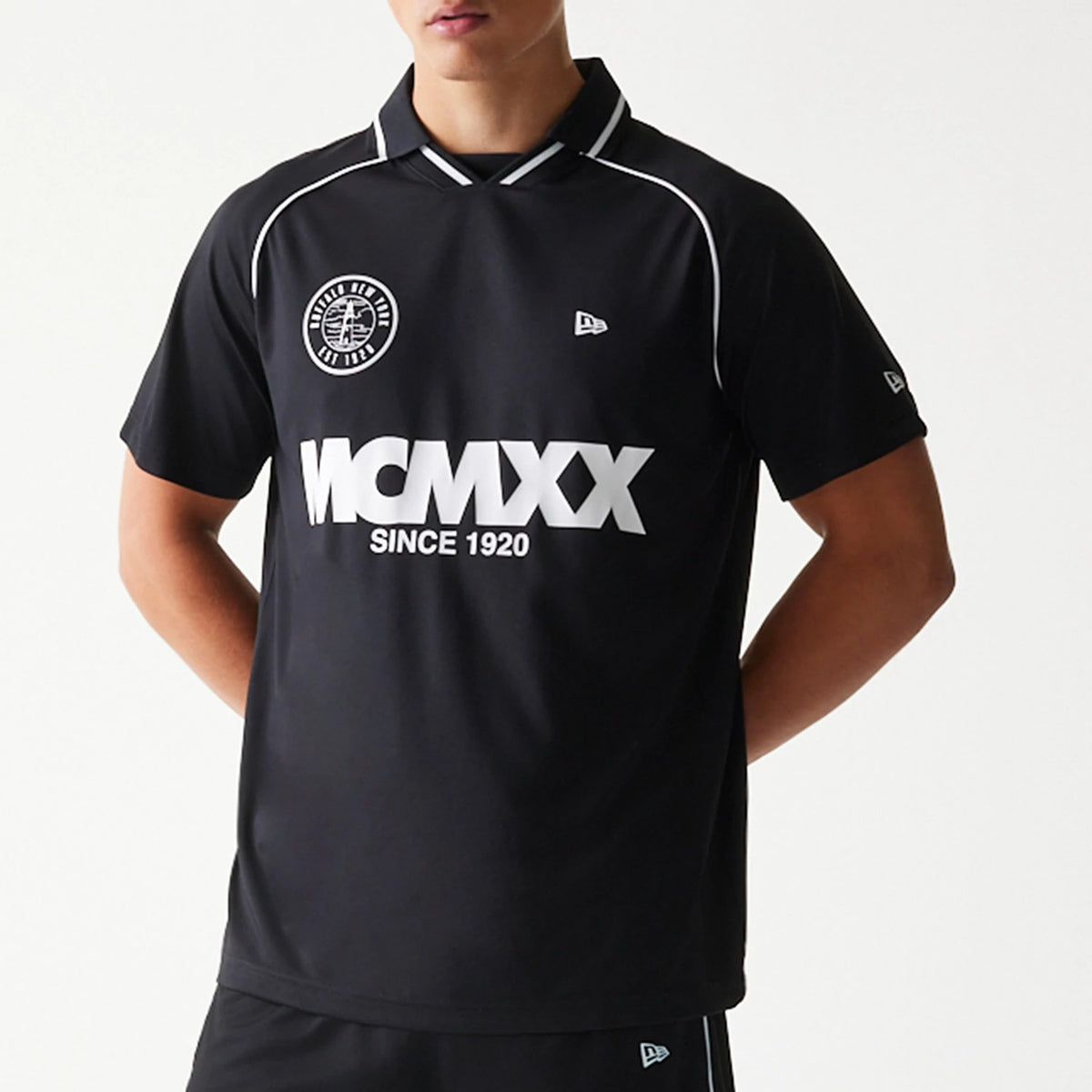New Era Football Black T-Shirt, front view on a model showing the white printed MCMXX Since 1920 text across the chest, embroidered New Era logo on the left chest and sleeve, and contrasting white piping around the shoulders and collar.