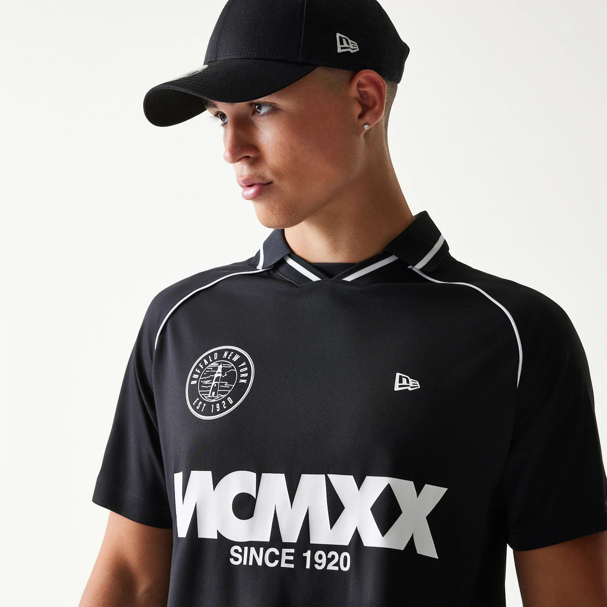 New Era Football Black T-Shirt, front view on a model with a black cap, featuring a white embroidered New Era logo on the chest, Buffalo New York Est 1920 circular graphic on the upper left, and WCMXW since 1920 in lettering below.