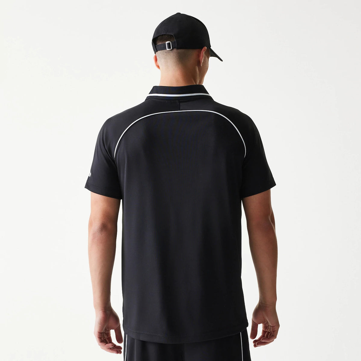 New Era Football Black T-Shirt, back view on a model with a black cap, showing a white piping detail curving across the upper back and the plain black fabric extending down to the straight hem.