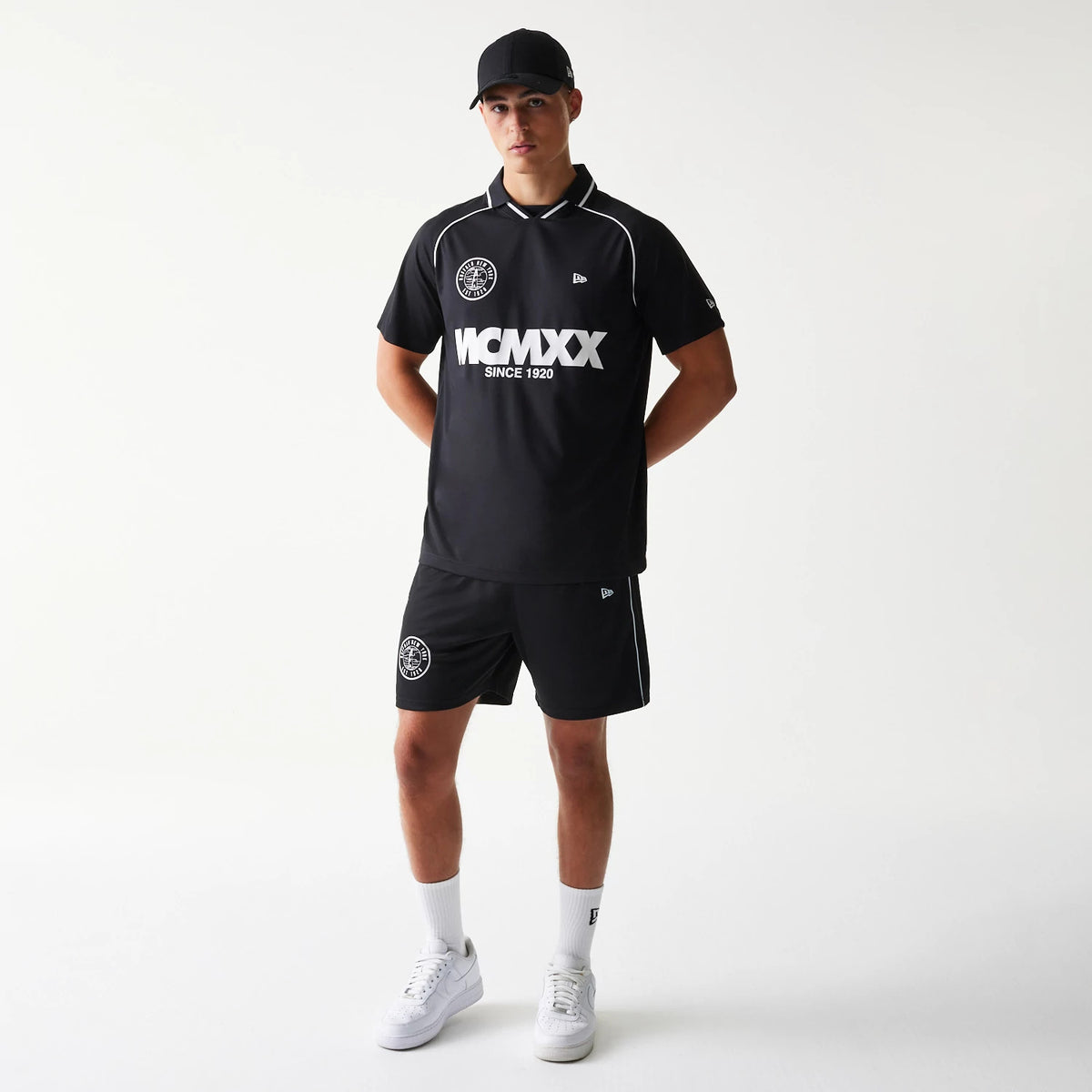 New Era Football Black T-Shirt, front view on-model displaying the white MCMLXX lettering and logo across the chest, a small embroidered New Era logo on the sleeve, and white piping along the collar and sleeves.