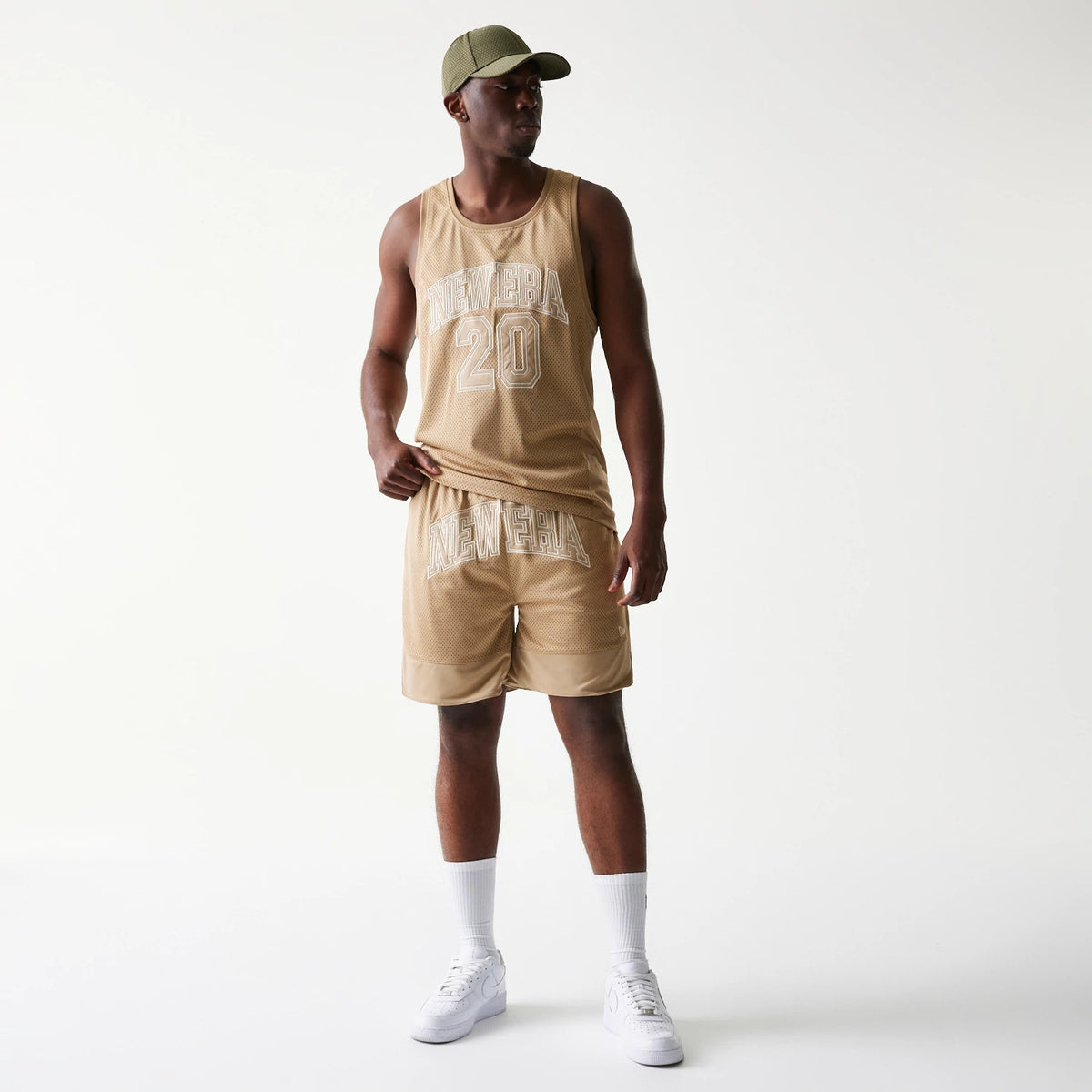 New Era Mesh Graphic Light Beige Oversized Shorts, on-model view showing matching light beige tank top with large embroidered New Era 20 graphic on the front, styled with a coordinating cap and white trainers.