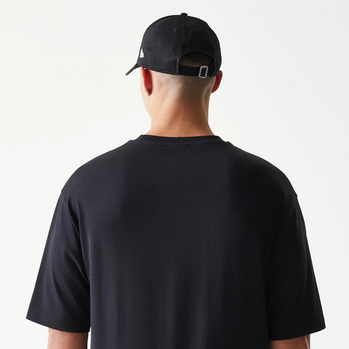 New Era Lemon Fruit Graphic Black Oversized T-Shirt, back view on a model paired with a black cap, showing a clean black design with no graphics, emphasising the loose fit and short sleeves.