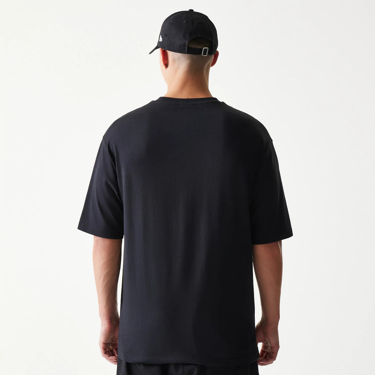 New Era Lemon Fruit Graphic Black Oversized T-Shirt, back view showing the plain black oversized fit with a relaxed drop-shoulder sleeve design, no graphics, worn with a black cap featuring an embroidered New Era logo on the side.