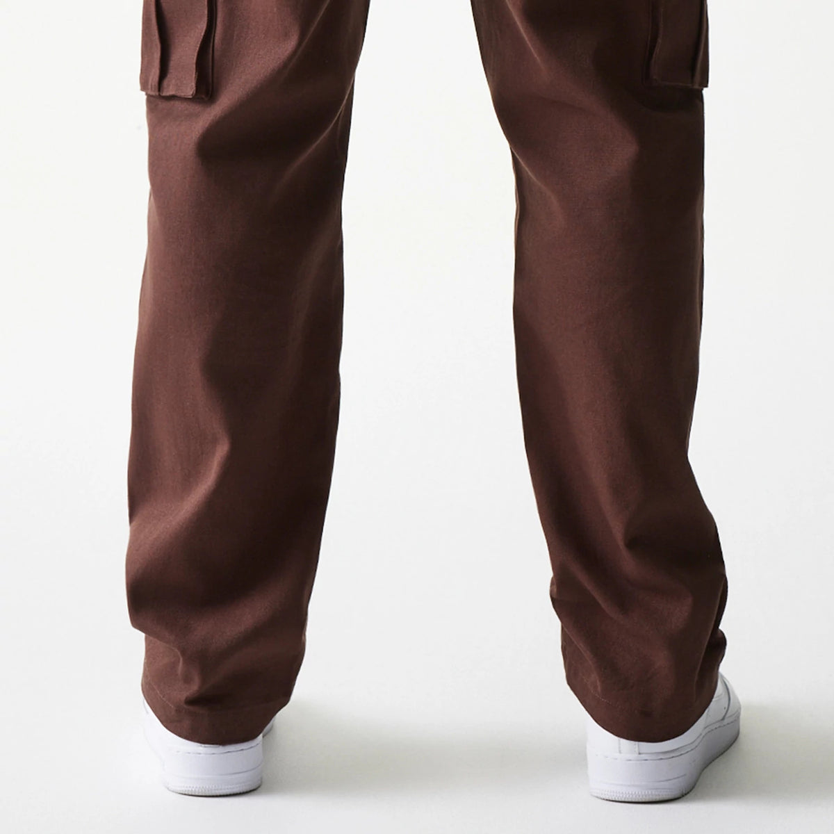 New Era Brown Straight Leg Cargo Joggers, rear view on a model showing the relaxed fit and straight leg design in brown fabric, with the hem falling over white trainers and a side pocket flap on the left leg.