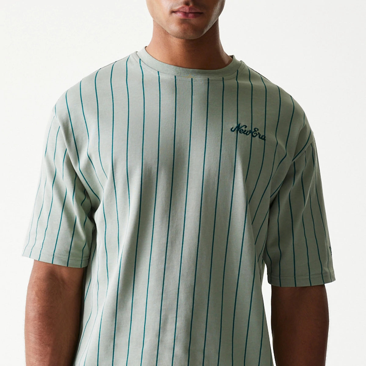 New Era Pinstripe Pastel Green Oversized T-Shirt, front view on-model displaying vertical blue pinstripes across the light green fabric with an embroidered New Era logo on the left chest.