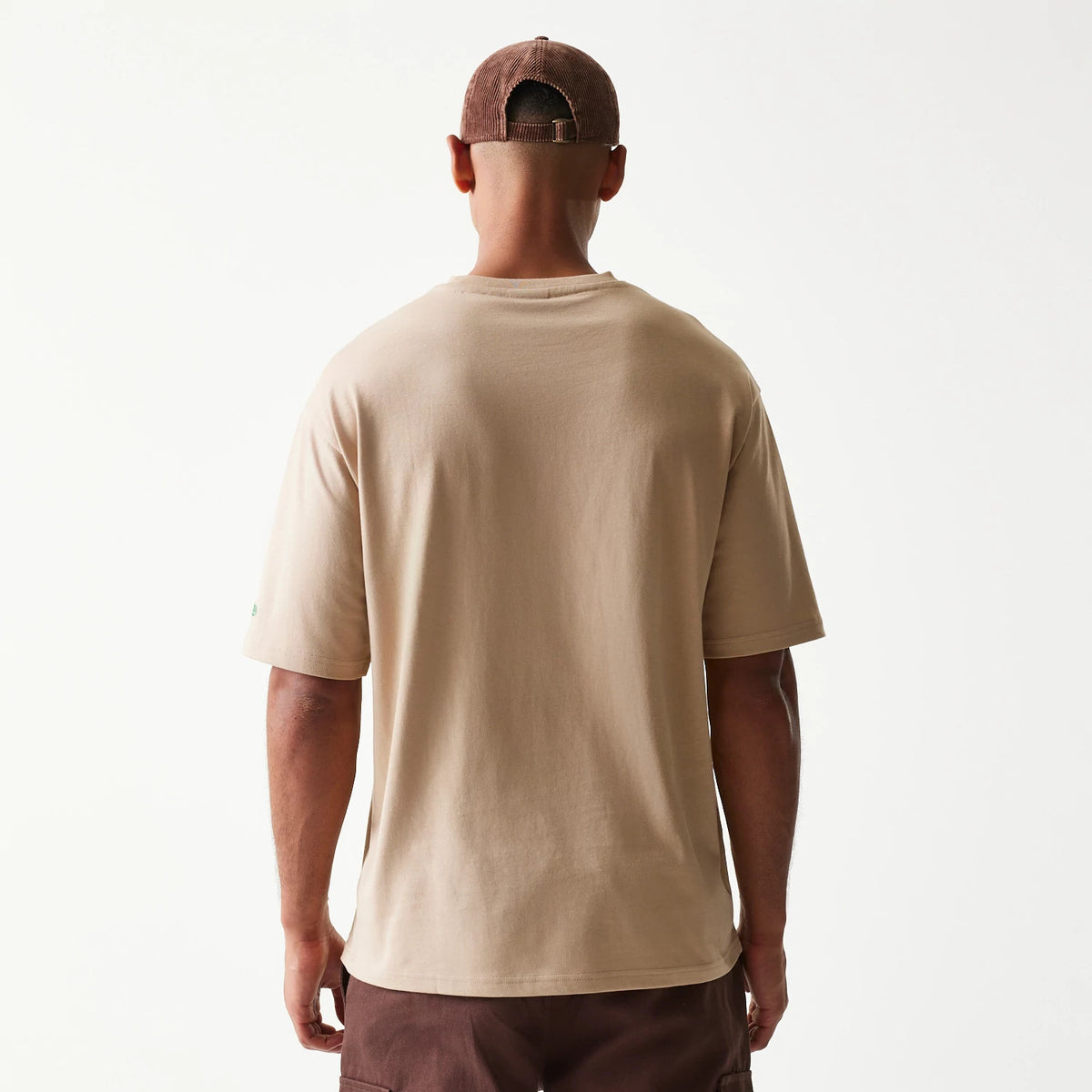 New Era Orange Fruit Graphic Light Beige Oversized T-Shirt, back view on a model wearing a brown cap, showing the plain light beige back and the relaxed oversized fit of the short sleeves.