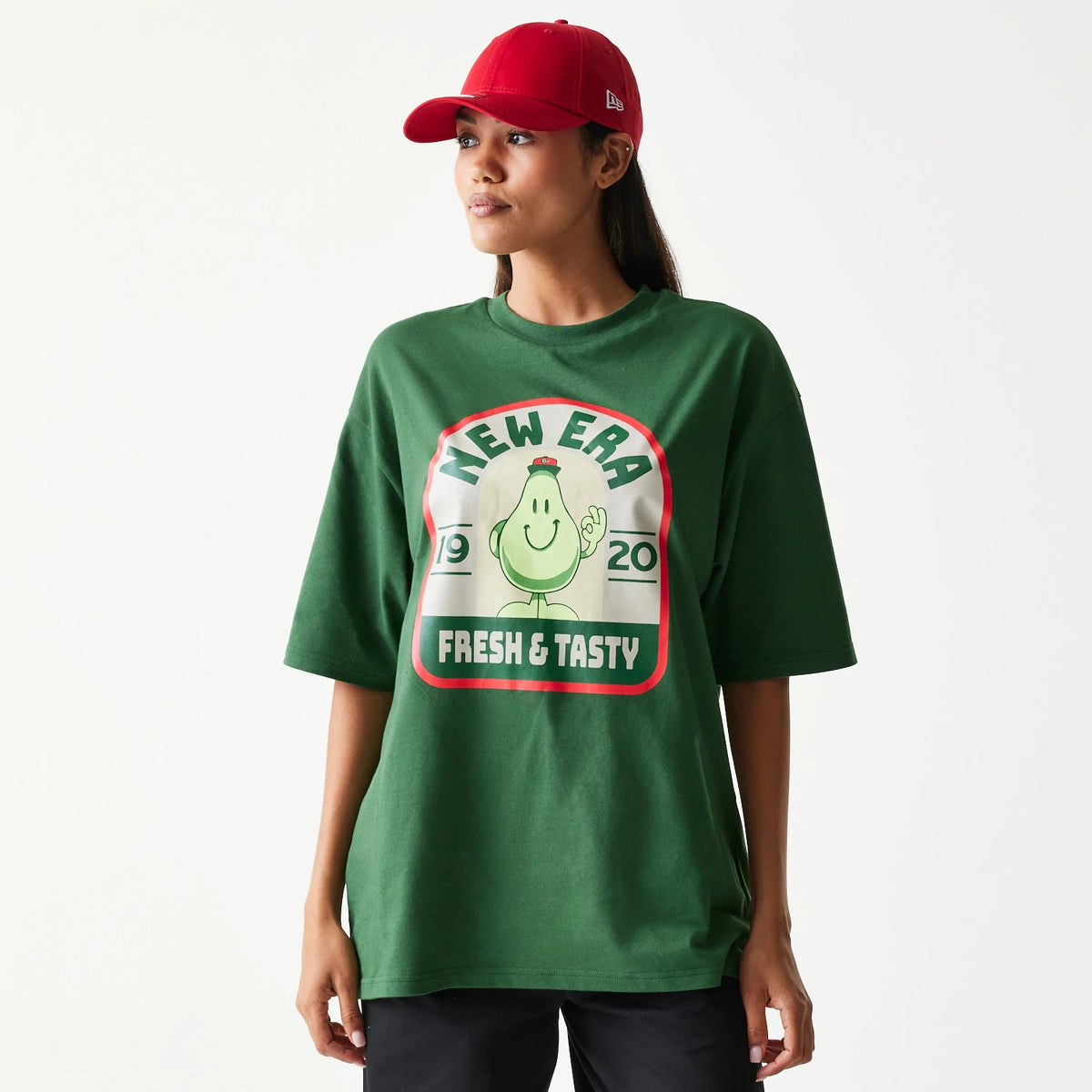 New Era Pear Fruit Graphic Dark Green Oversized T-Shirt, front view on-model featuring a large central graphic of a smiling pear with text New Era Fresh & Tasty 1920 in a red-bordered square, styled with a red cap.