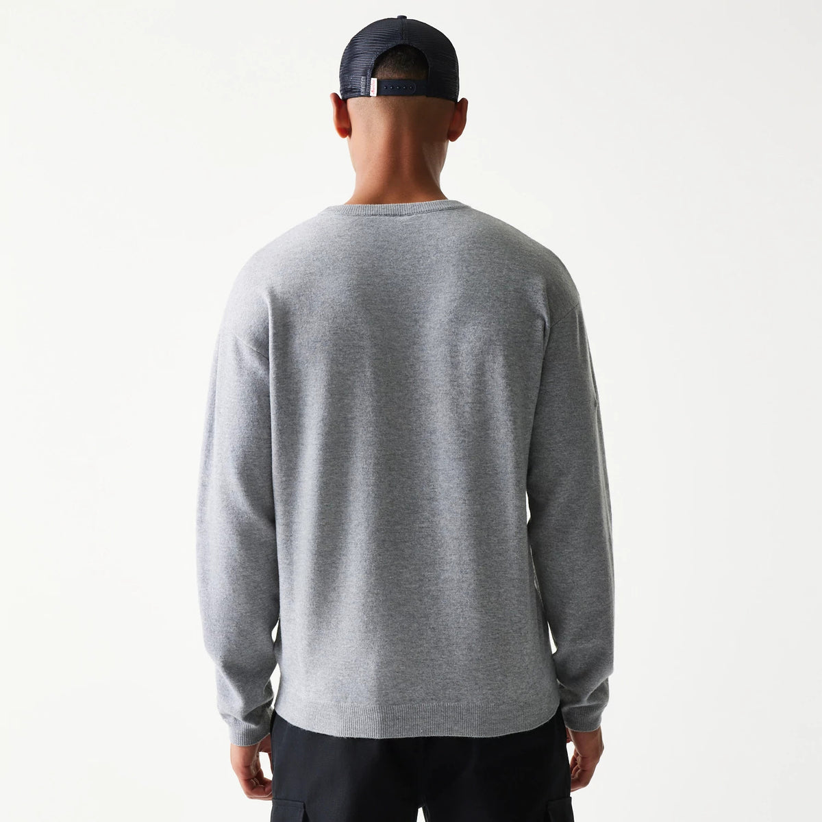 New Era Essential Flag Grey Knitted Sweater, back view on a model showing the plain light grey design with ribbed cuffs and hem, displaying a relaxed fit against black trousers.
