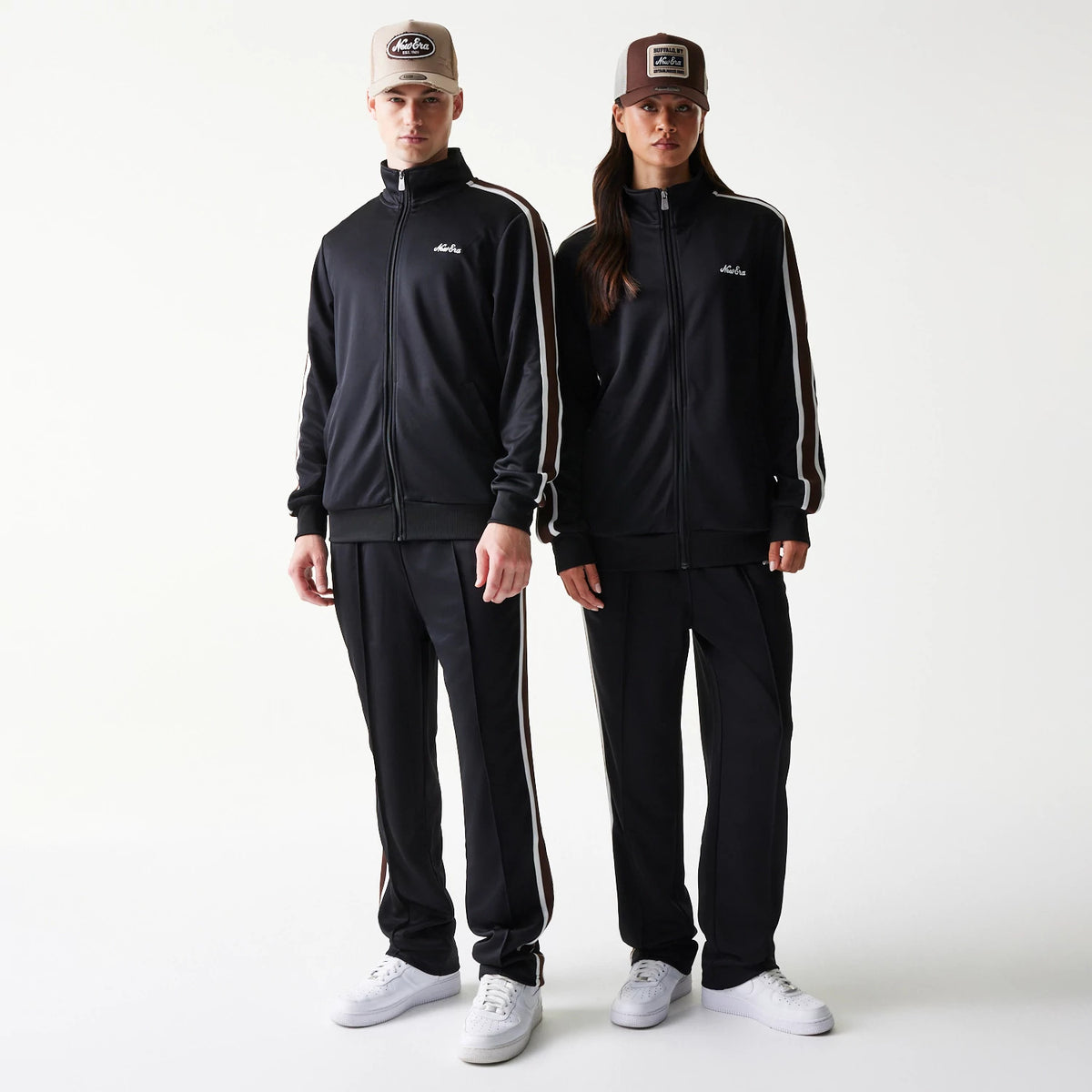 New Era Script Black Track Jacket, front view on models with matching caps, featuring a solid black body with white stripe details along the sleeves and an embroidered script logo on the left chest.