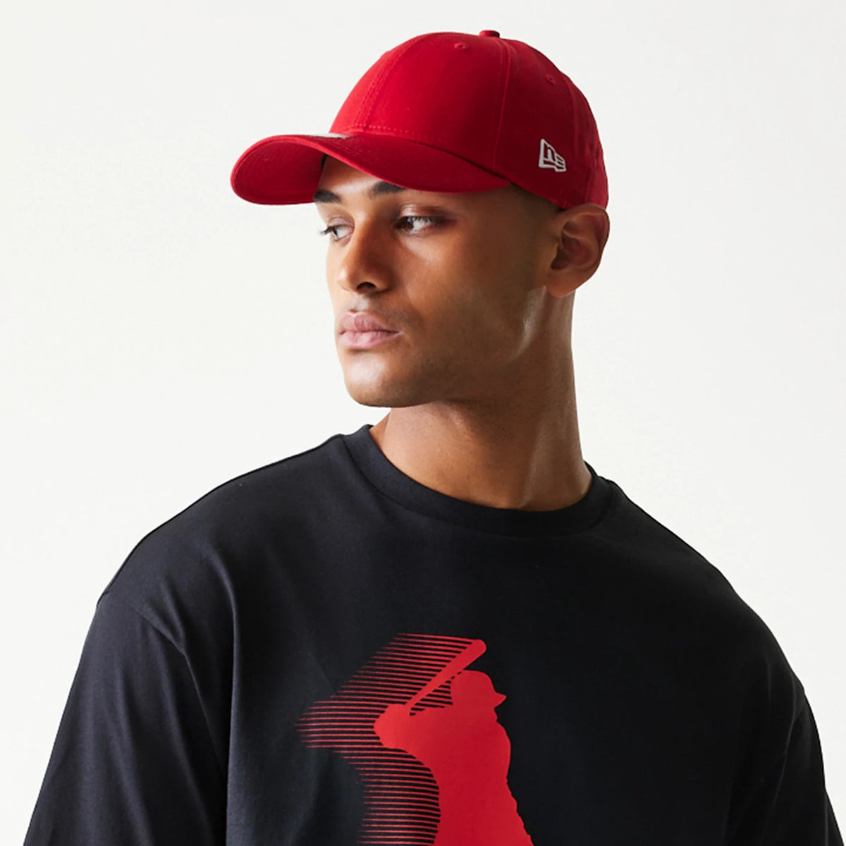 New Era Baseball Player Graphic Black Oversized T-Shirt, front view on a model wearing a red cap, displaying a red silhouette graphic of a baseball player swinging a bat on the chest centre.