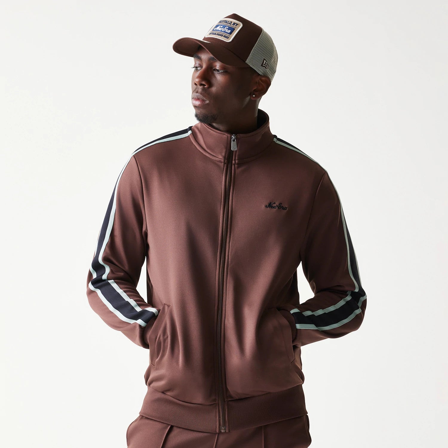 New Era Script Brown Track Jacket, front view on-model featuring a high collar, full zip closure, side stripes on the sleeves, and an embroidered black New Era logo on the left chest.