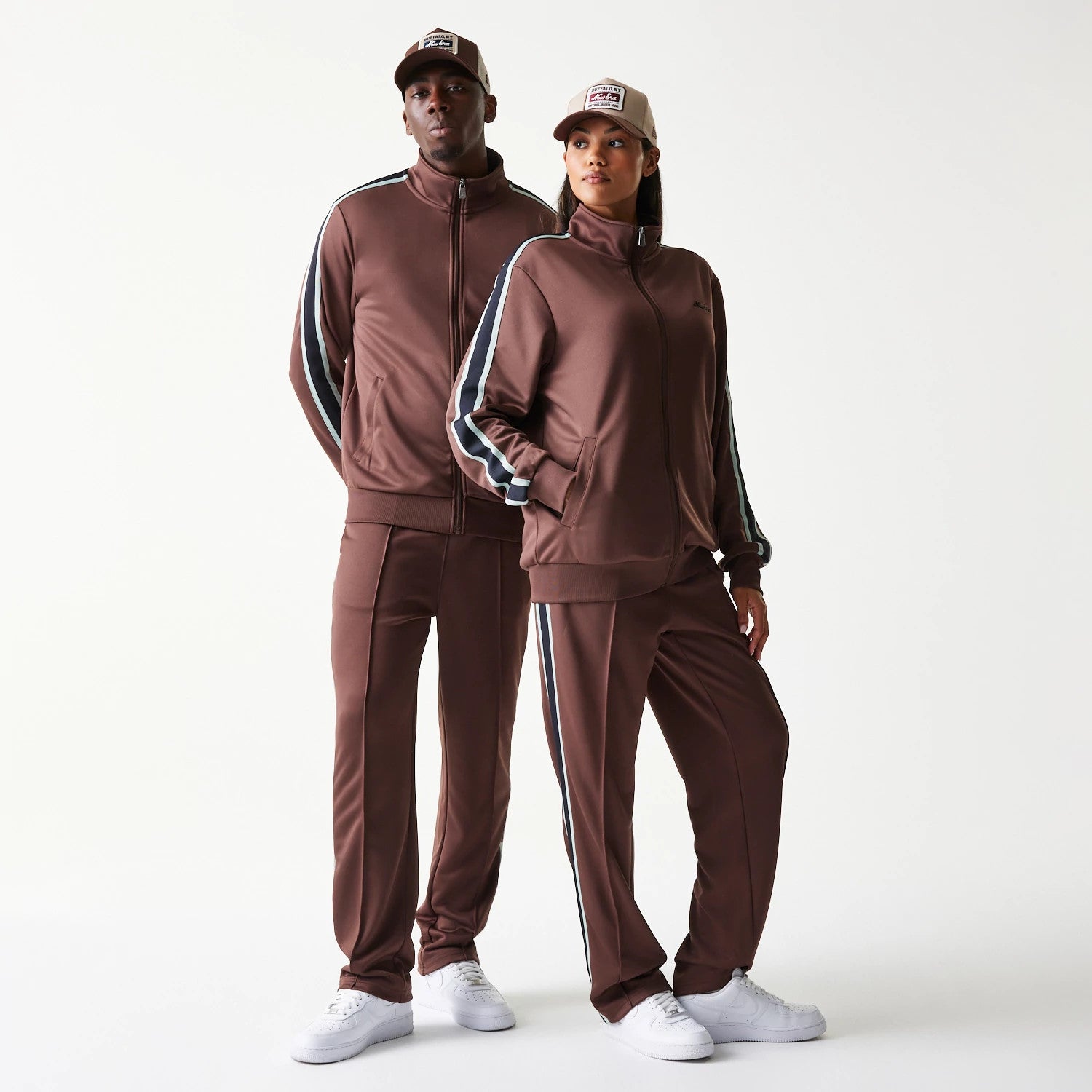 New Era Script Brown Track Jacket, front view on-model showing the brown jacket with a central zip, high collar, and contrasting stripes along the sleeves, paired with matching track pants and a neutral cap.