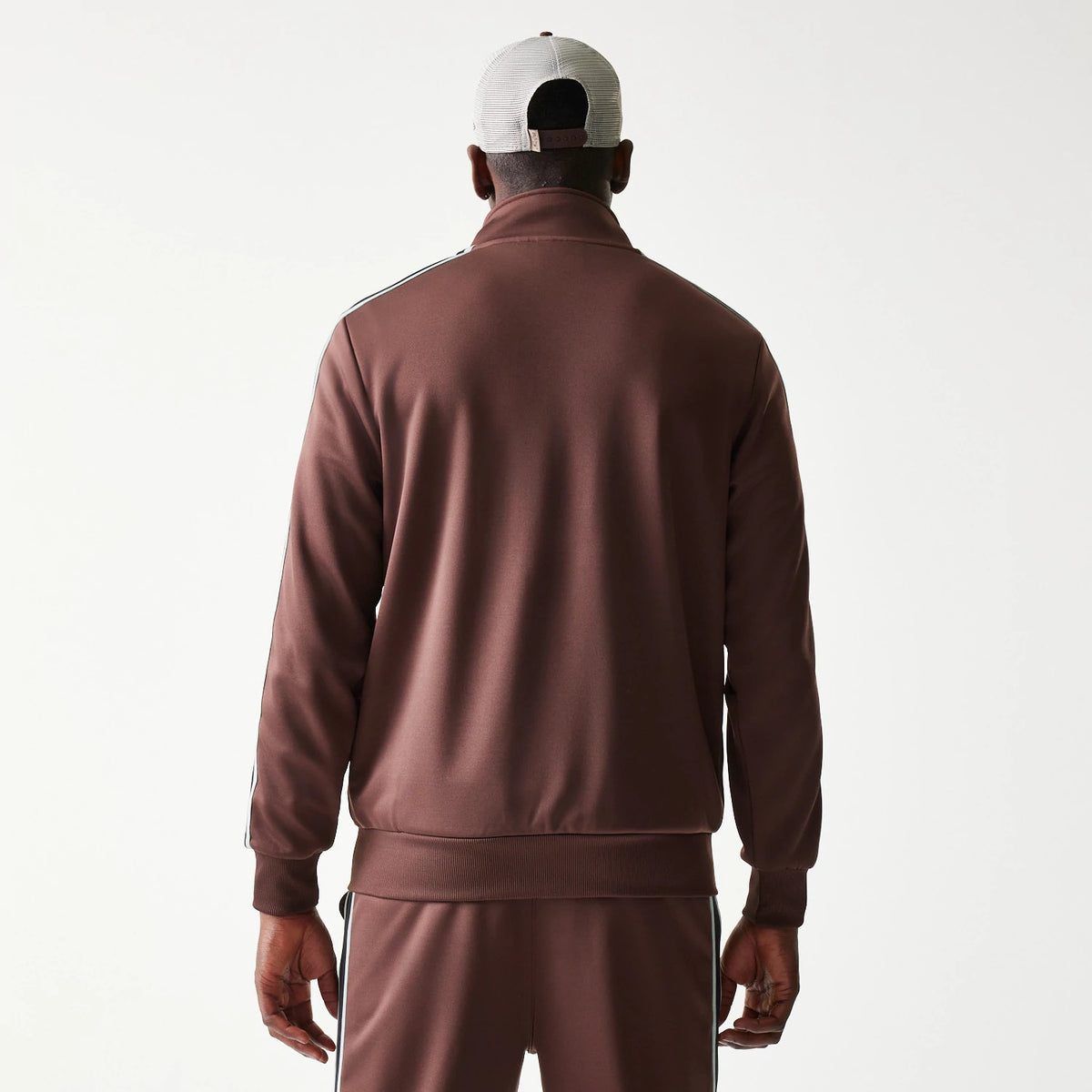 New Era Script Brown Track Jacket, back view on-model showing a plain brown back with piping along the shoulders and sleeves, paired with brown track bottoms and a light-coloured cap.