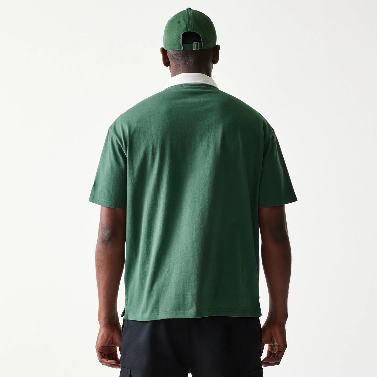 New Era LA Dodgers MLB Dark Green Oversized Polo T-Shirt, back view on-model showcasing the plain dark green back with short sleeves, under a white collar, paired with a matching dark green cap displaying eyelets and an adjustable strap at the back.