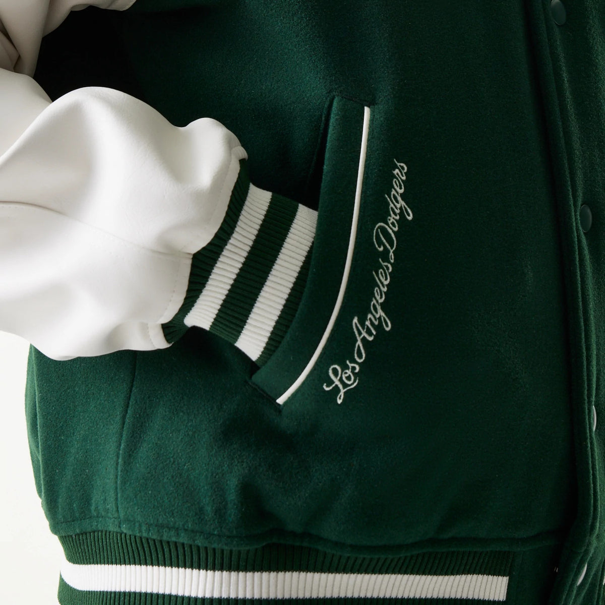 New Era LA Dodgers MLB Dark Green Varsity Jacket, three-quarter view showing the dark green body with white contrasting sleeves and a striped green and white cuff, a white embroidered Los Angeles Dodgers script near the pocket.