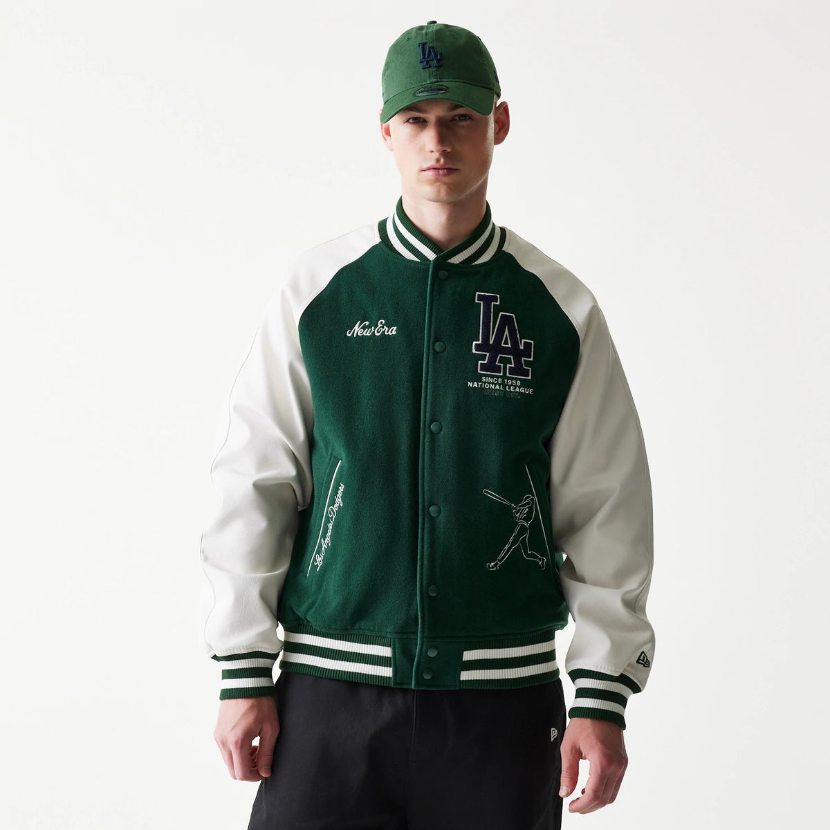 New Era LA Dodgers MLB Dark Green Varsity Jacket, front view on-model displaying a large embroidered LA logo on the left chest, a New Era logo on the right, and contrasting white sleeves, paired with a matching green cap.