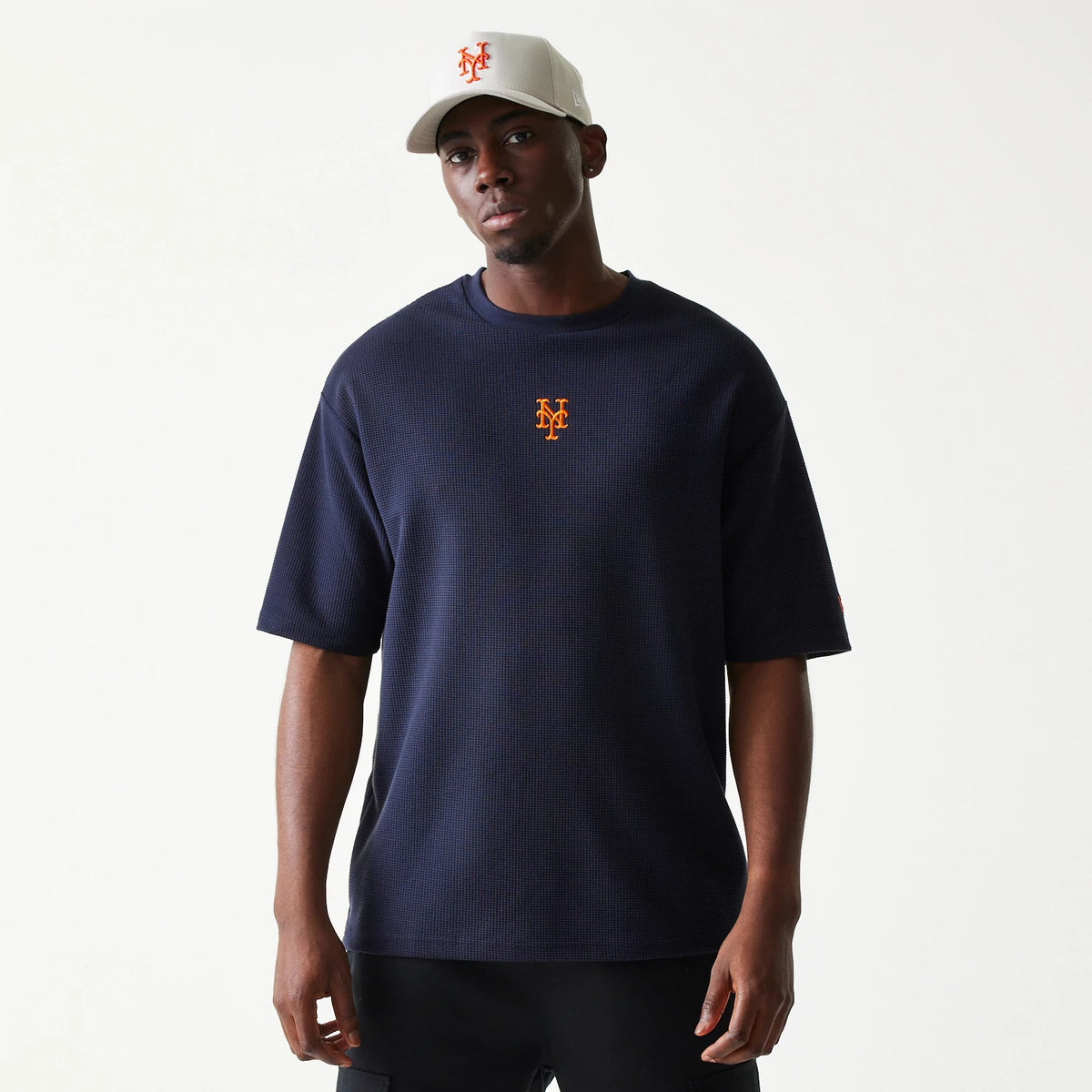 New Era New York Mets MLB Waffle Navy Oversized T-Shirt, front view on-model displaying the orange embroidered Mets logo at the centre of the chest, styled with a matching white cap featuring the same orange logo.